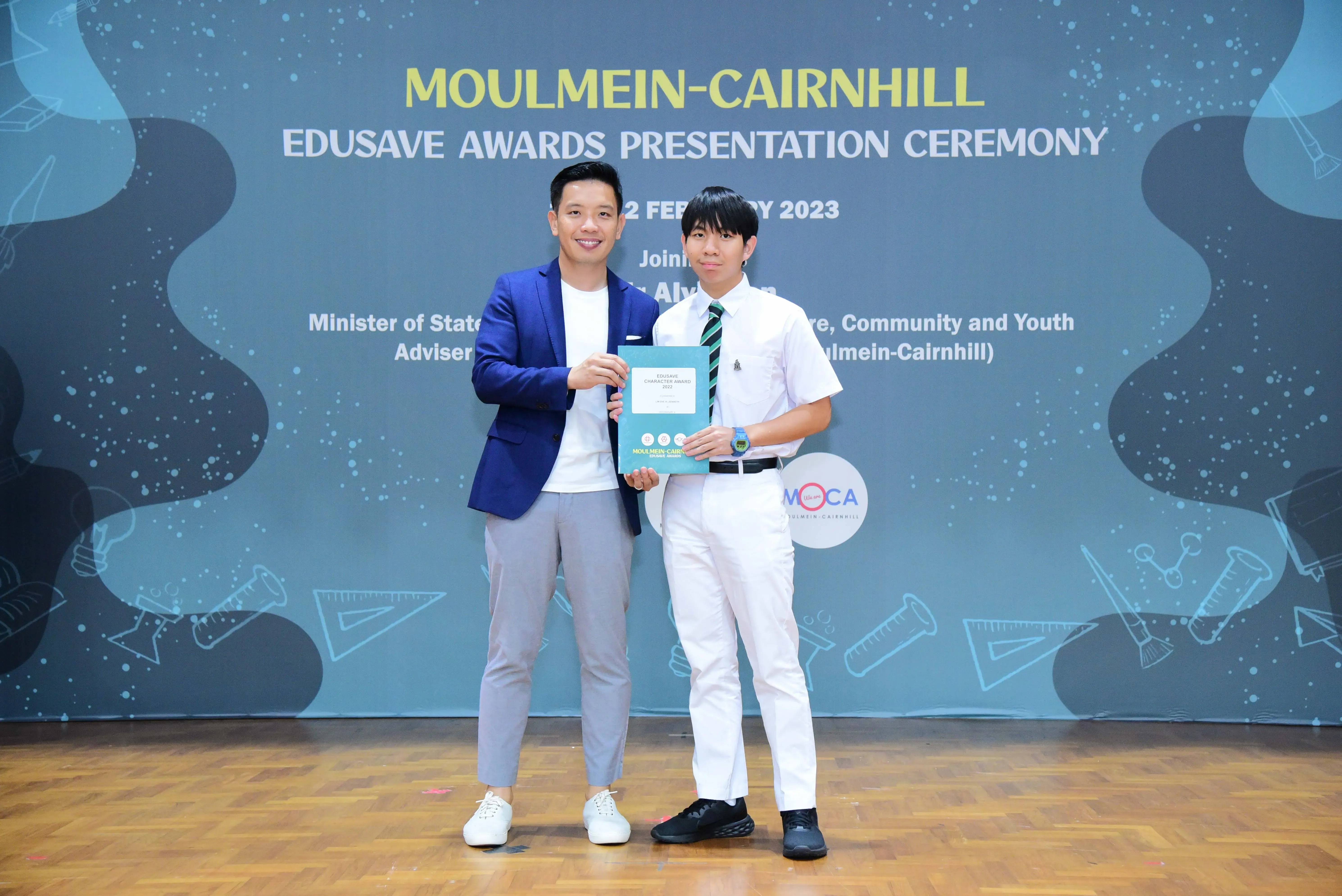 Two men hold a certificate together at the Moulmein-Cairnhill Edusave Awards Presentation Ceremony in 2023.