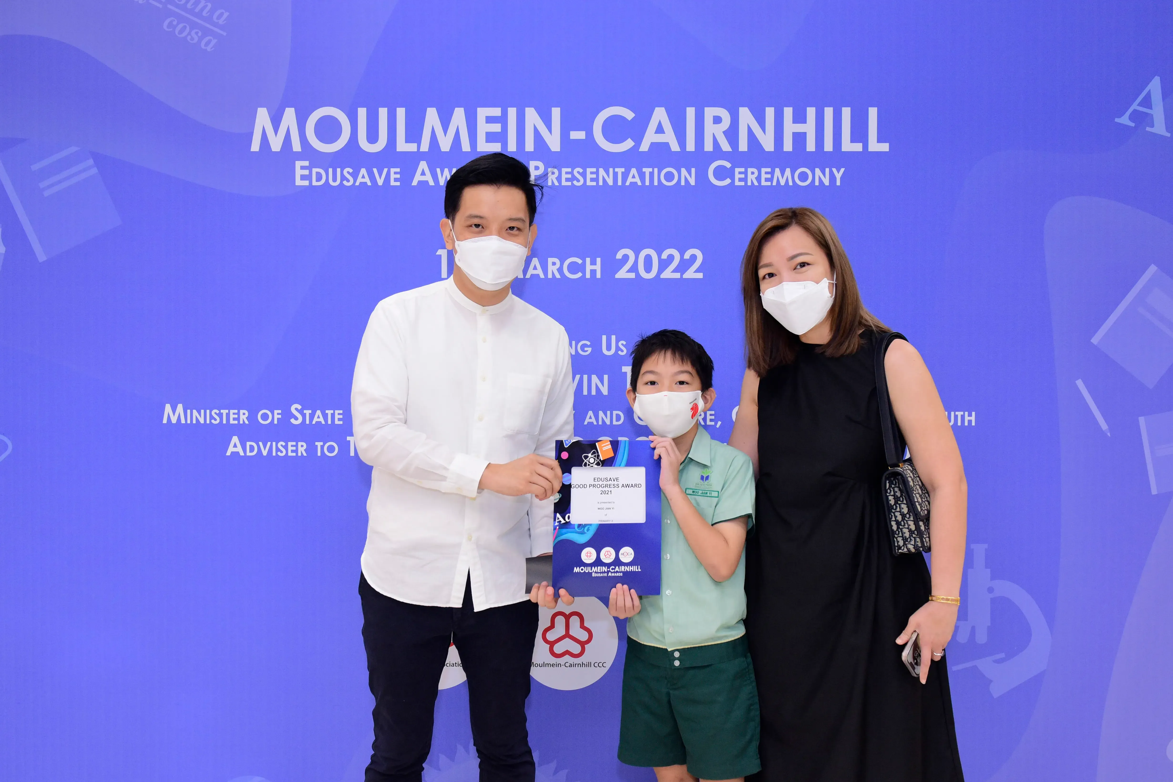 Two masked adults and a masked child hold an award at the Moulmein-Cairnhill Edusave Ceremony, March 2022.