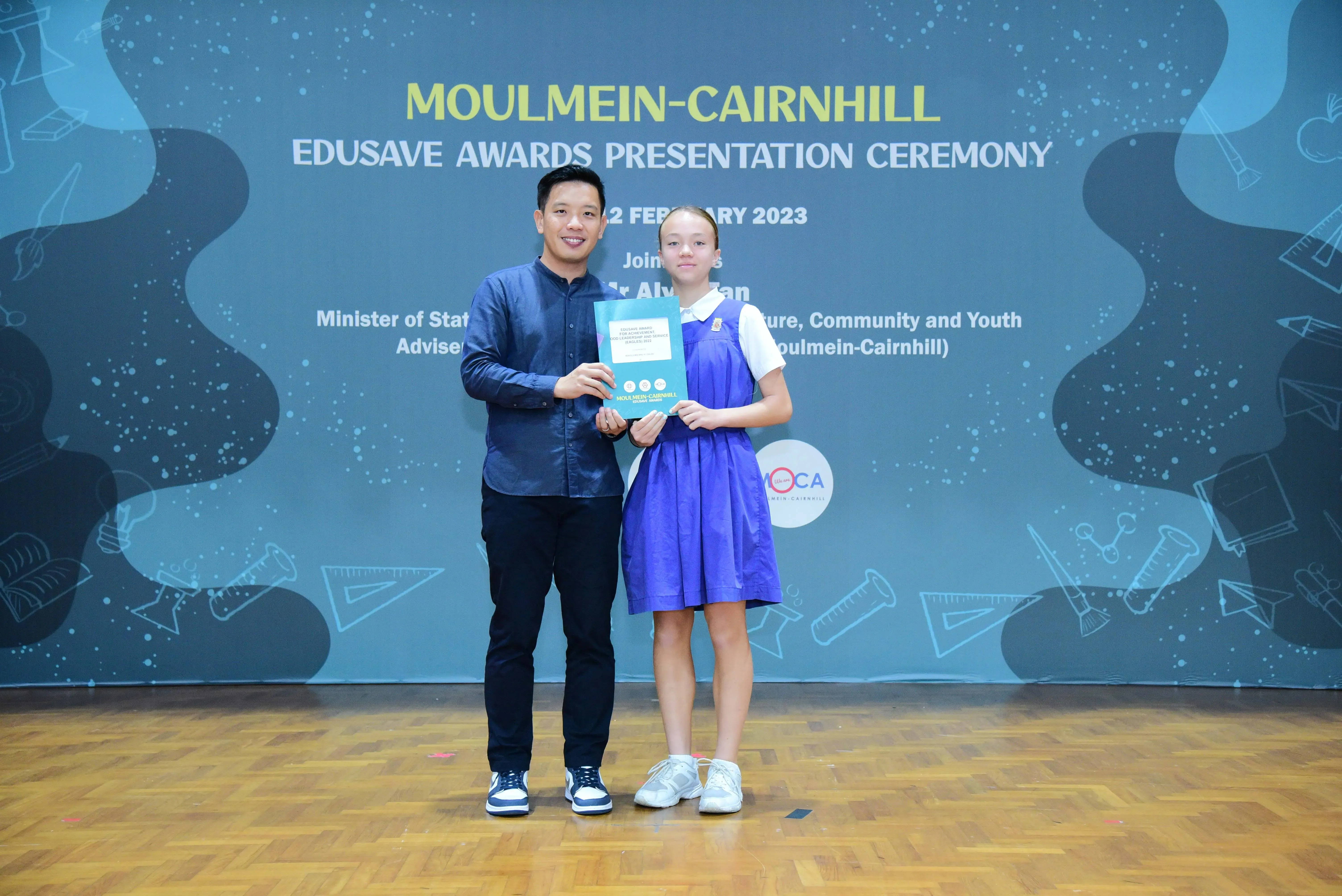A man and a young girl hold a certificate together at the Moulmein-Cairnhill Edusave Awards Ceremony 2023.