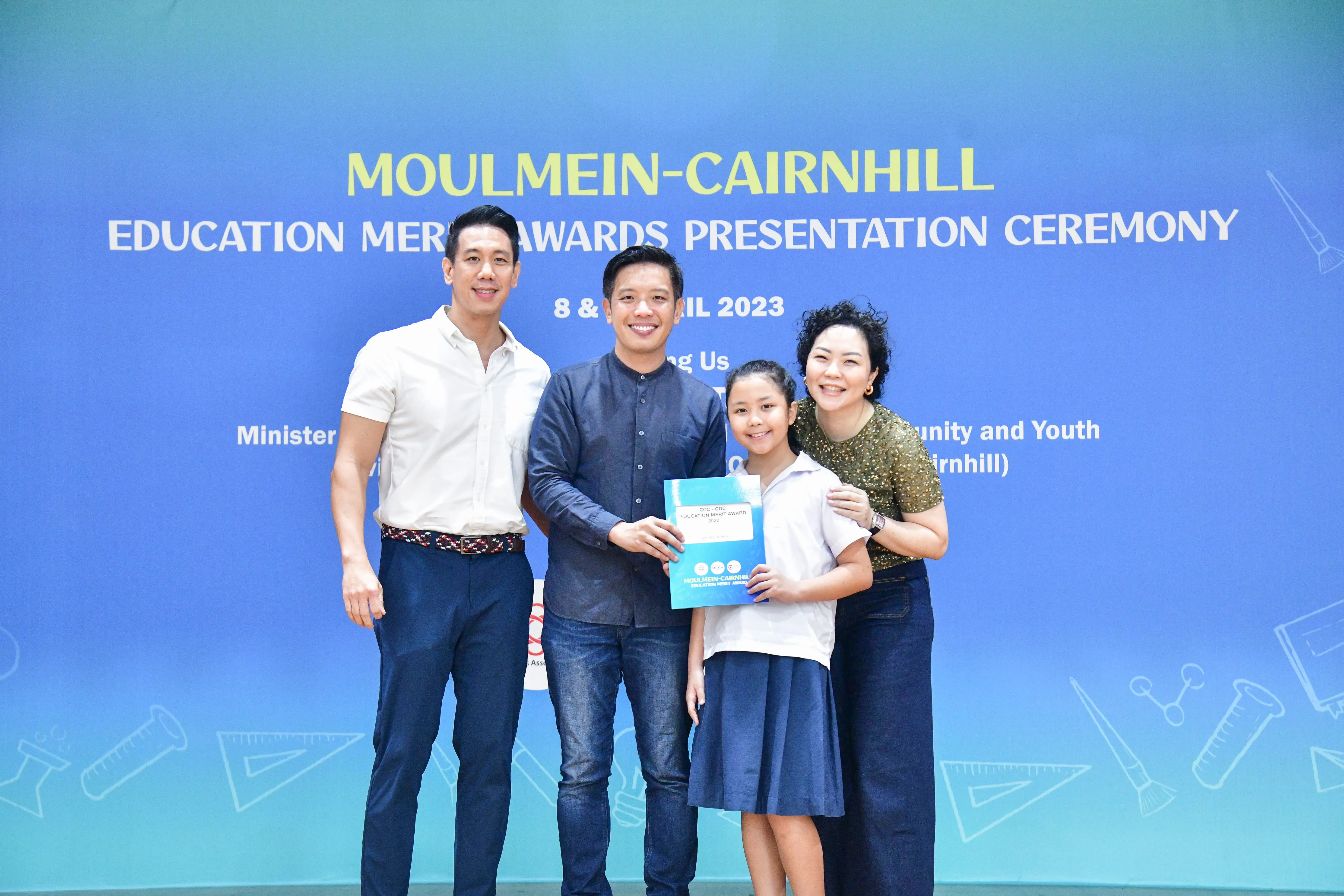 Three adults and a girl holding a certificate pose at the Moulmein-Cairnhill Education Merit Awards Ceremony 2023.