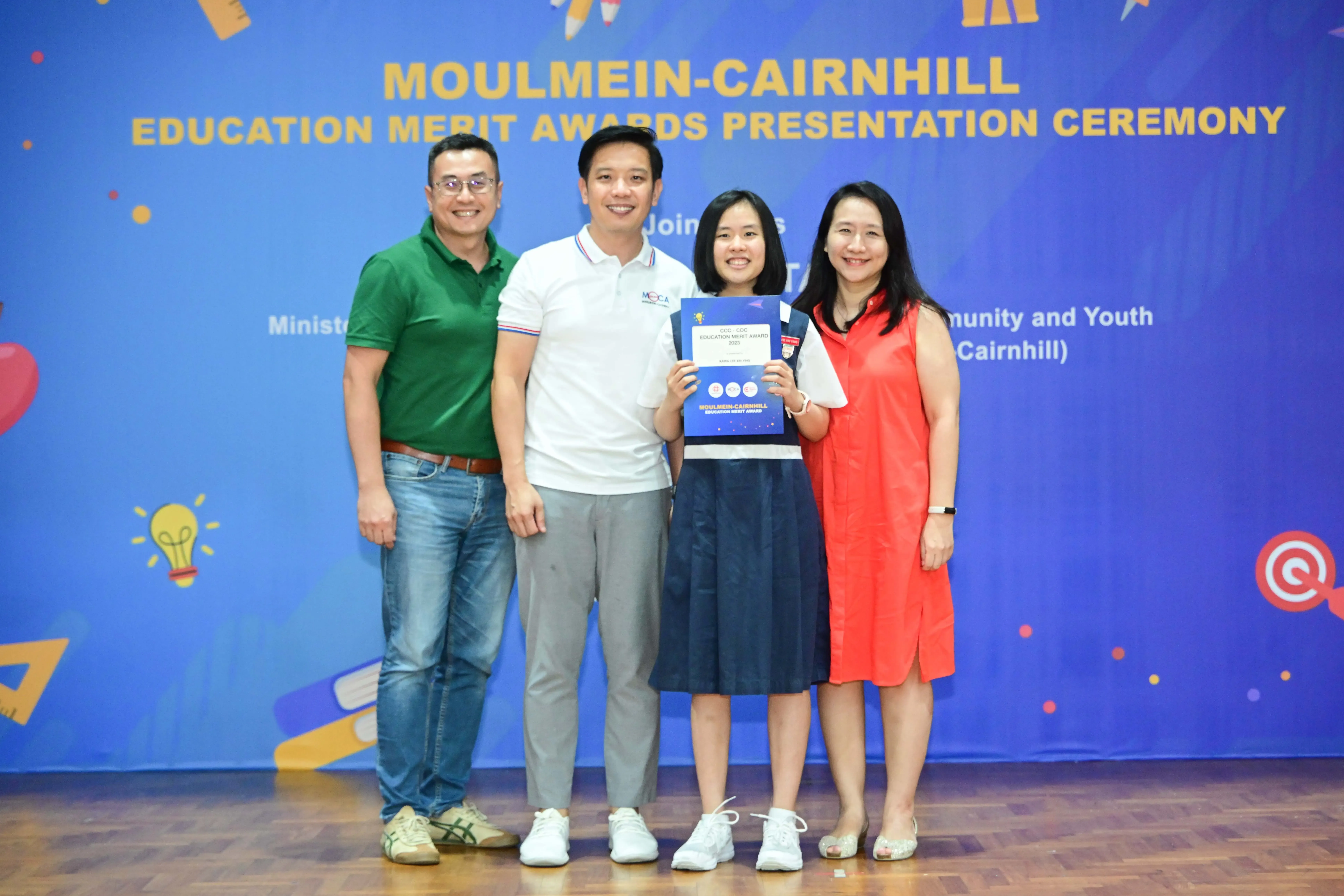 Four people posing at the Moulmein-Cairnhill Education Merit Awards Presentation Ceremony, one holding award certificates.
