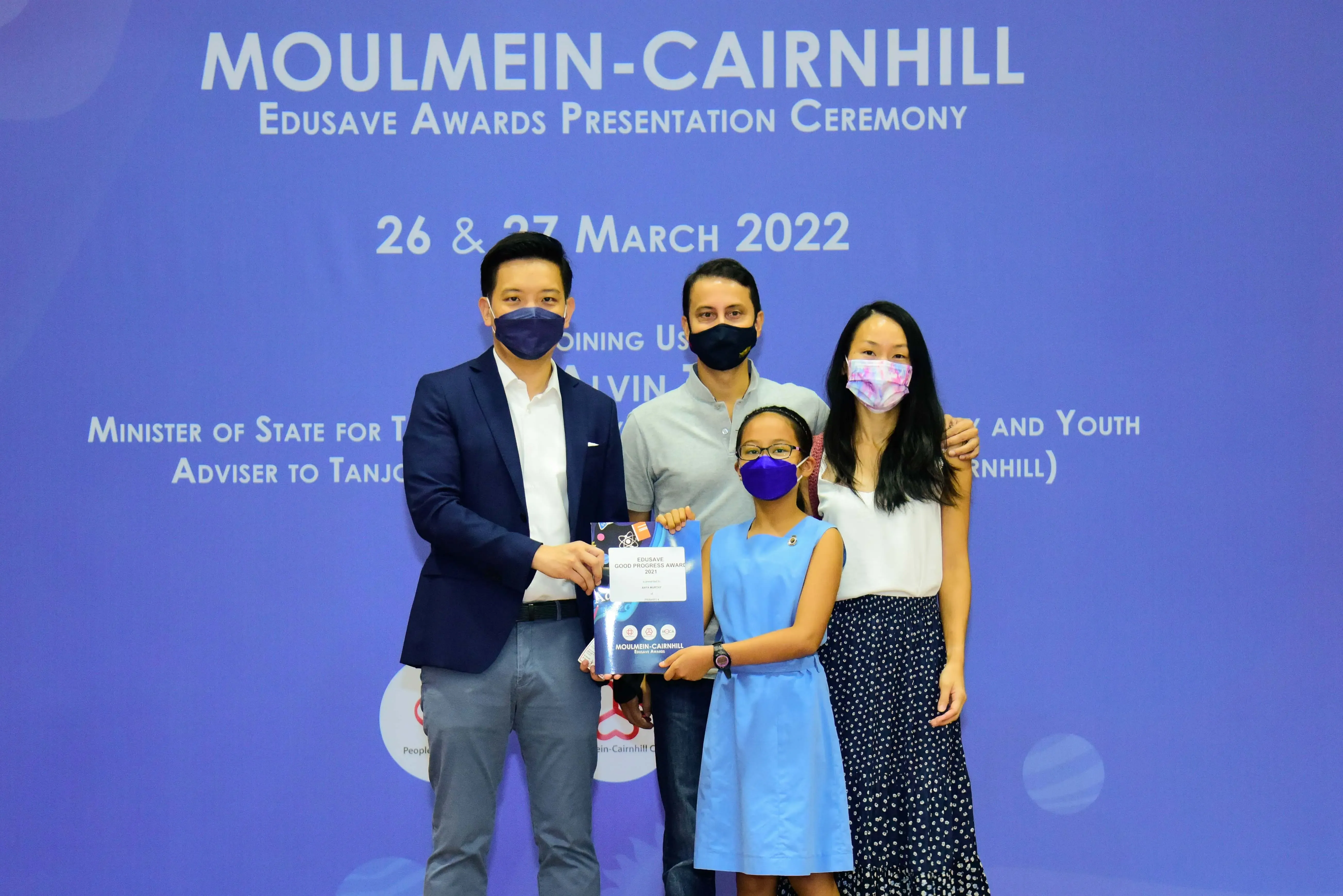 Four masked people pose at the Moulmein-Cairnhill Edusave Awards Ceremony on 26-27 March 2022, holding an award.