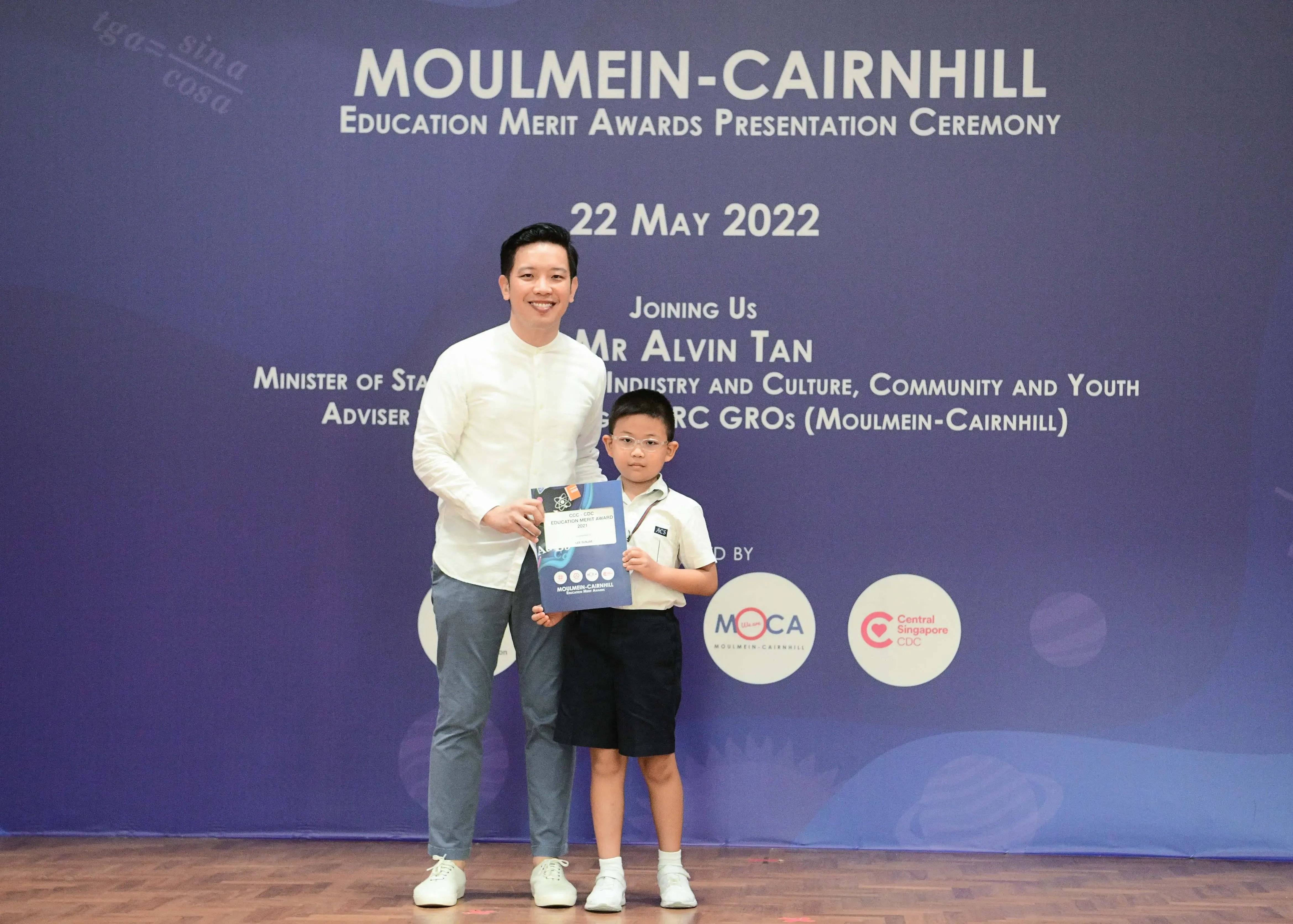 A man and a young boy hold a certificate at the Moulmein-Cairnhill Education Merit Awards Ceremony on 22 May 2022.