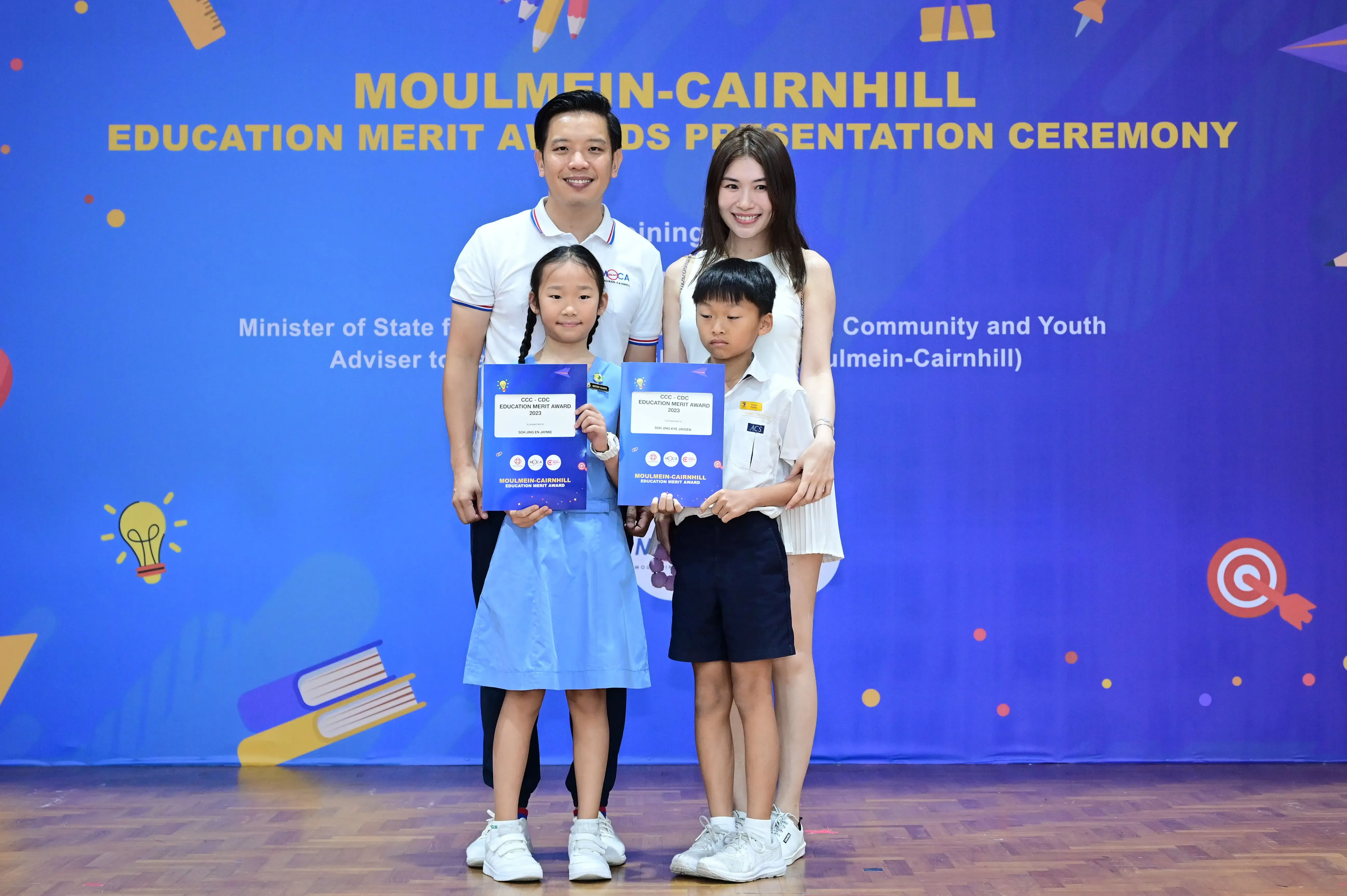 Two adults and two children pose with award certificates at the Moulmein-Cairnhill Education Merit Awards Ceremony.
