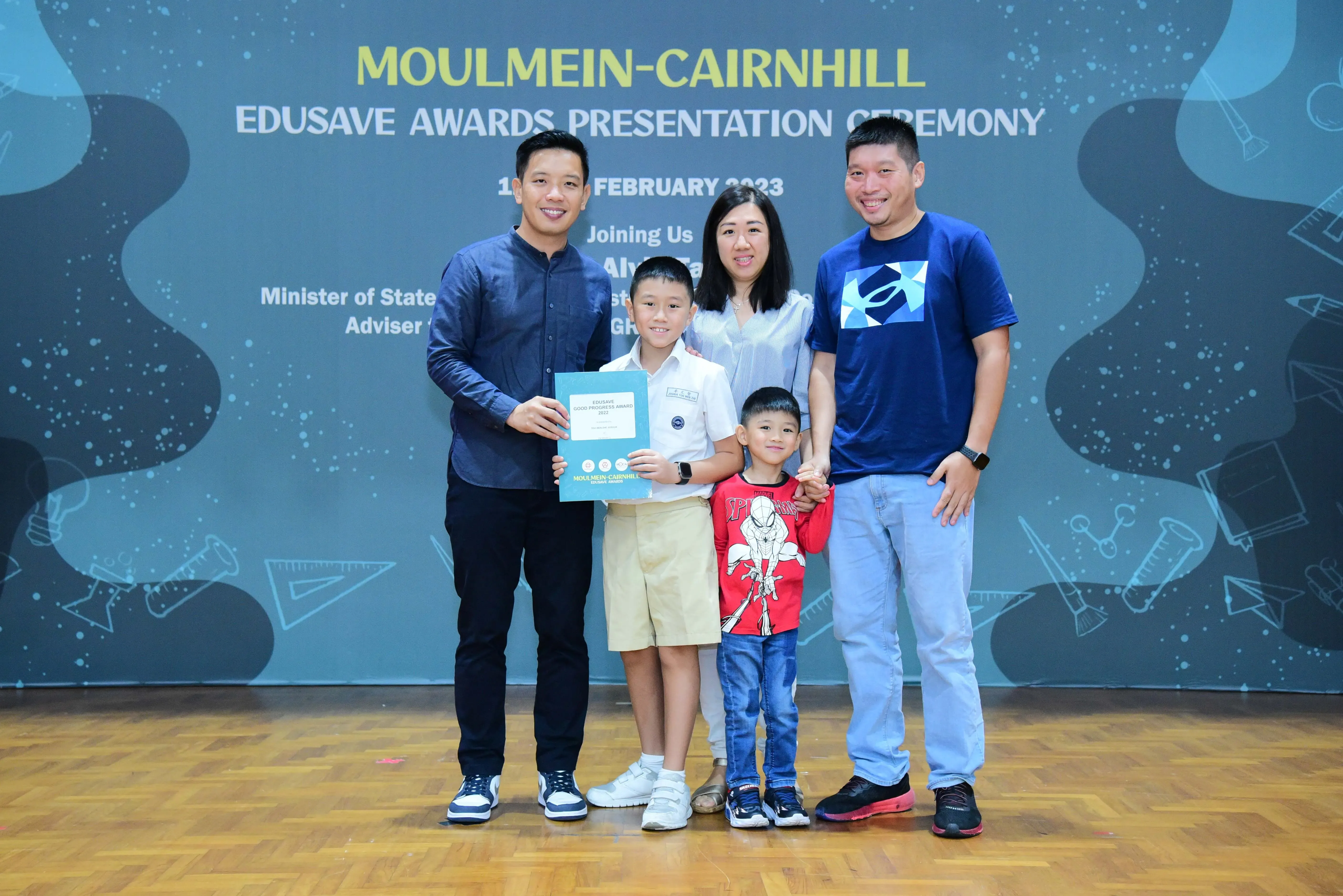 Five people pose at the Moulmein-Cairnhill Edusave Awards Ceremony, including a boy holding a certificate.