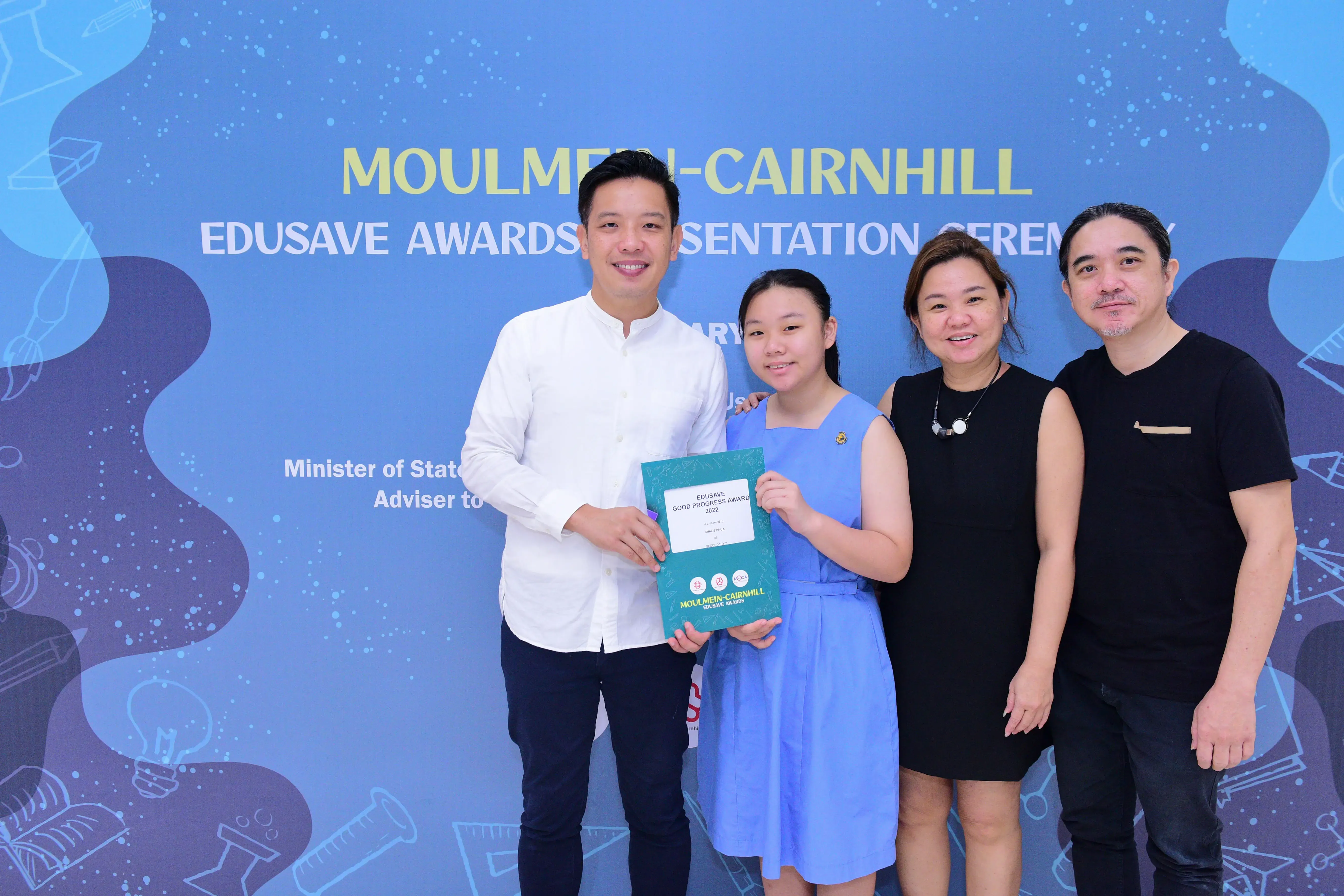 Four people pose holding an Edusave Good Progress Award certificate at the Moulmein-Cairnhill Edusave Awards Ceremony.