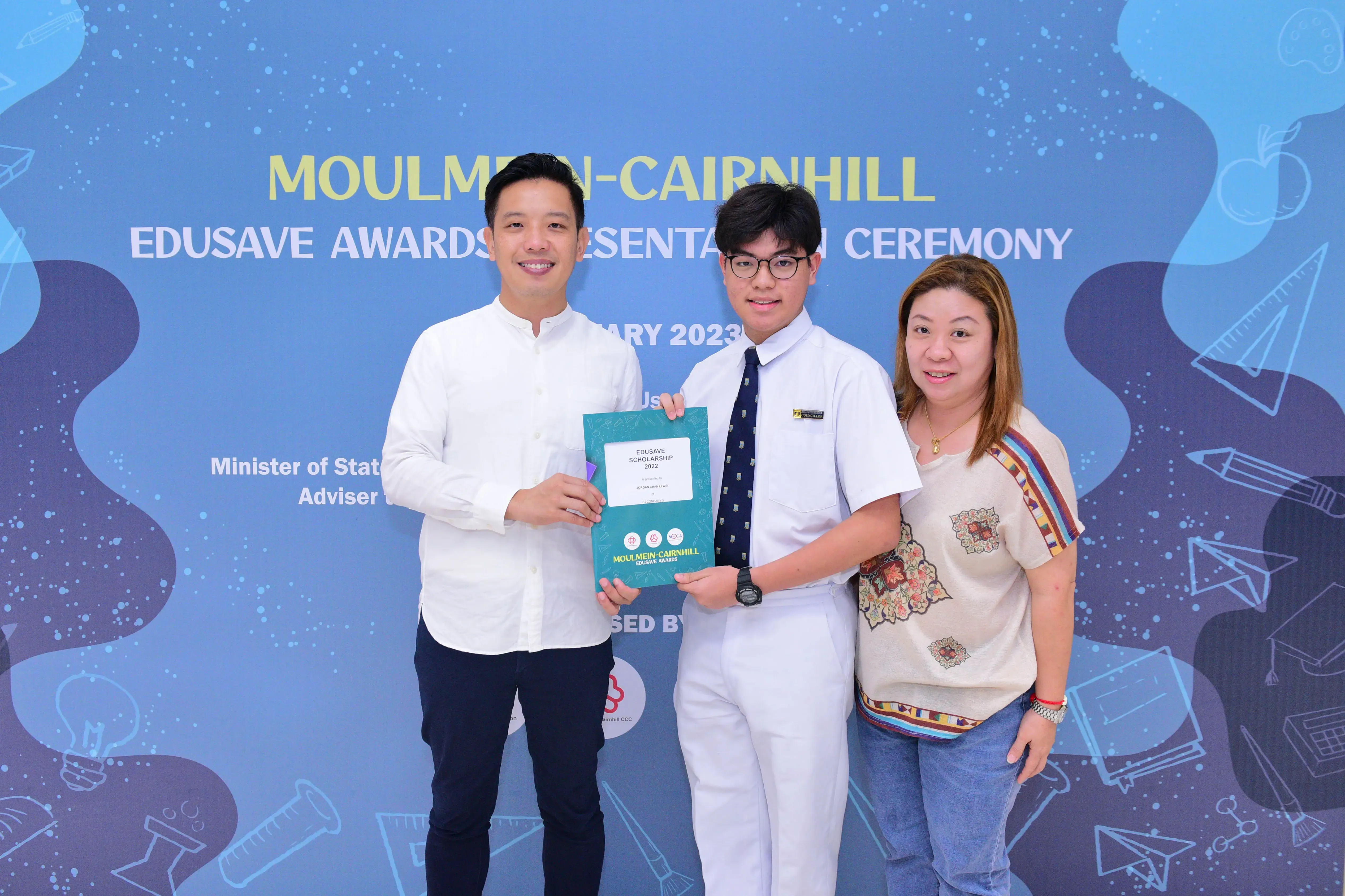 Three people pose holding an Edusave Scholarship certificate at the Moulmein-Cairnhill Awards Ceremony 2023.