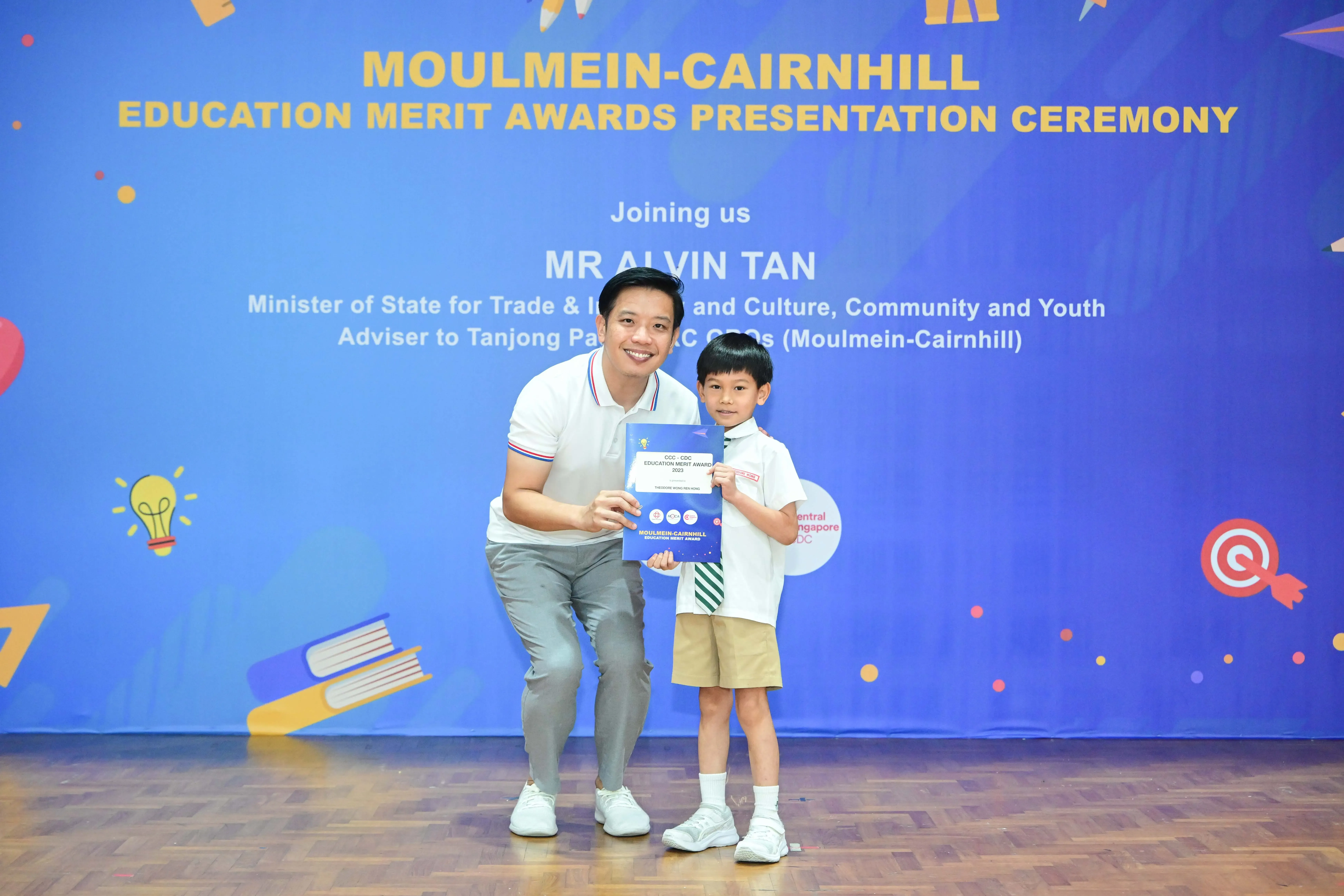 Man and young boy hold a certificate at the Moulmein-Cairnhill Education Merit Awards Presentation Ceremony.