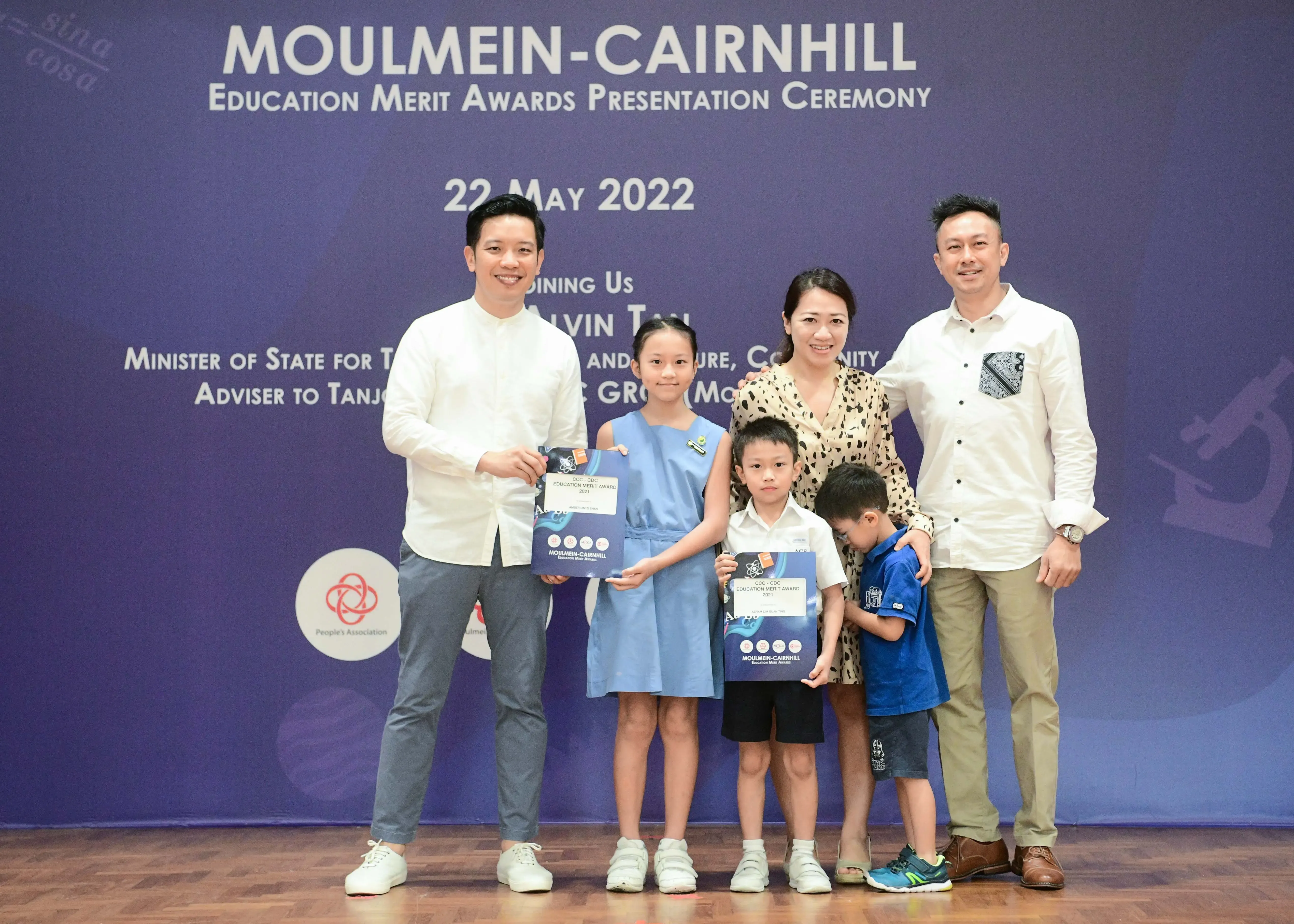 Group of adults and children posing with award certificates at Moulmein-Cairnhill Education Merit Awards Ceremony, May 2022.