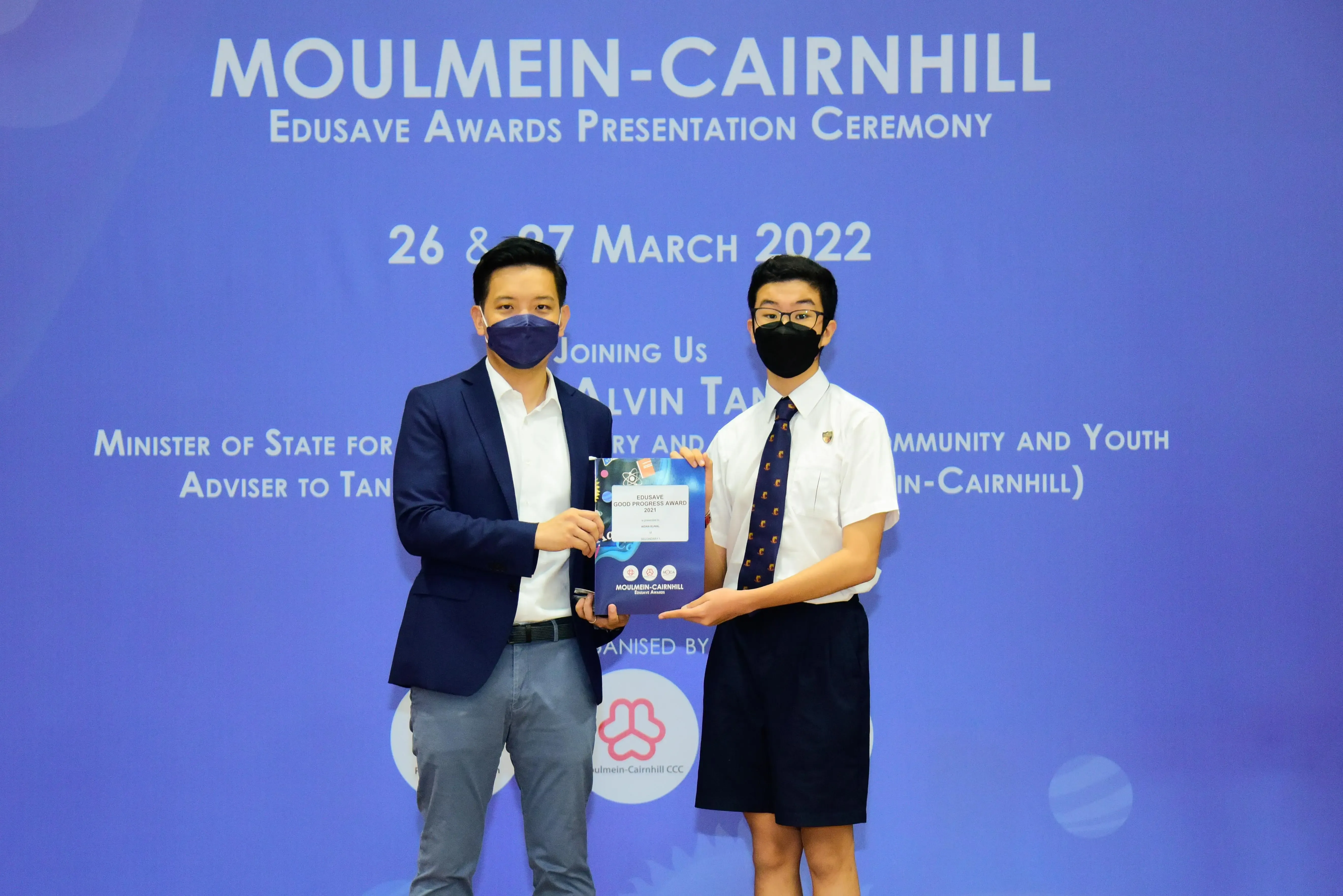 Two masked people hold an Edusave award certificate at the Moulmein-Cairnhill Awards Ceremony, March 2022.