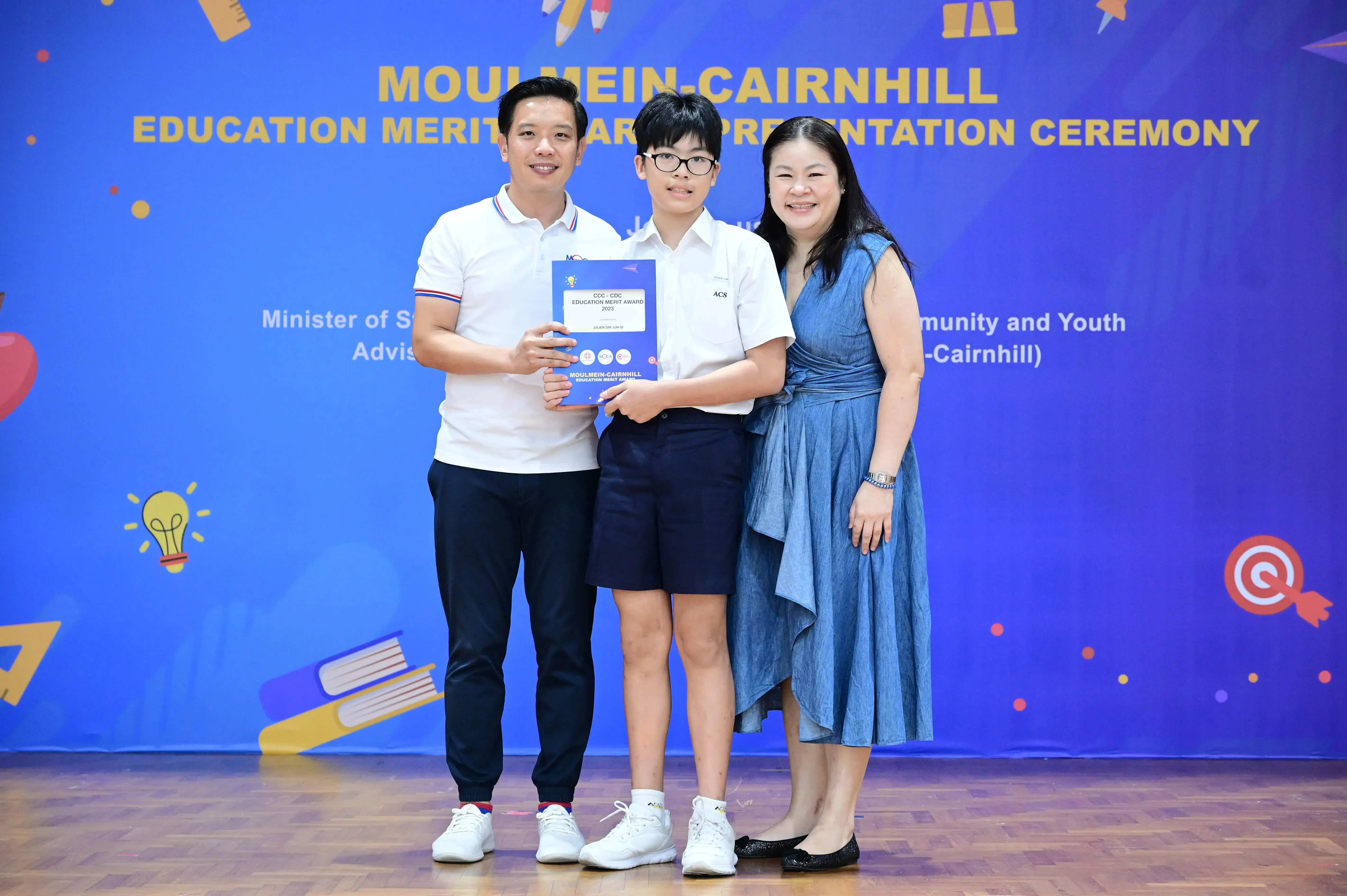 A boy holding a certificate poses with two adults at the Moulmein-Cairnhill Education Merit Award Presentation Ceremony.