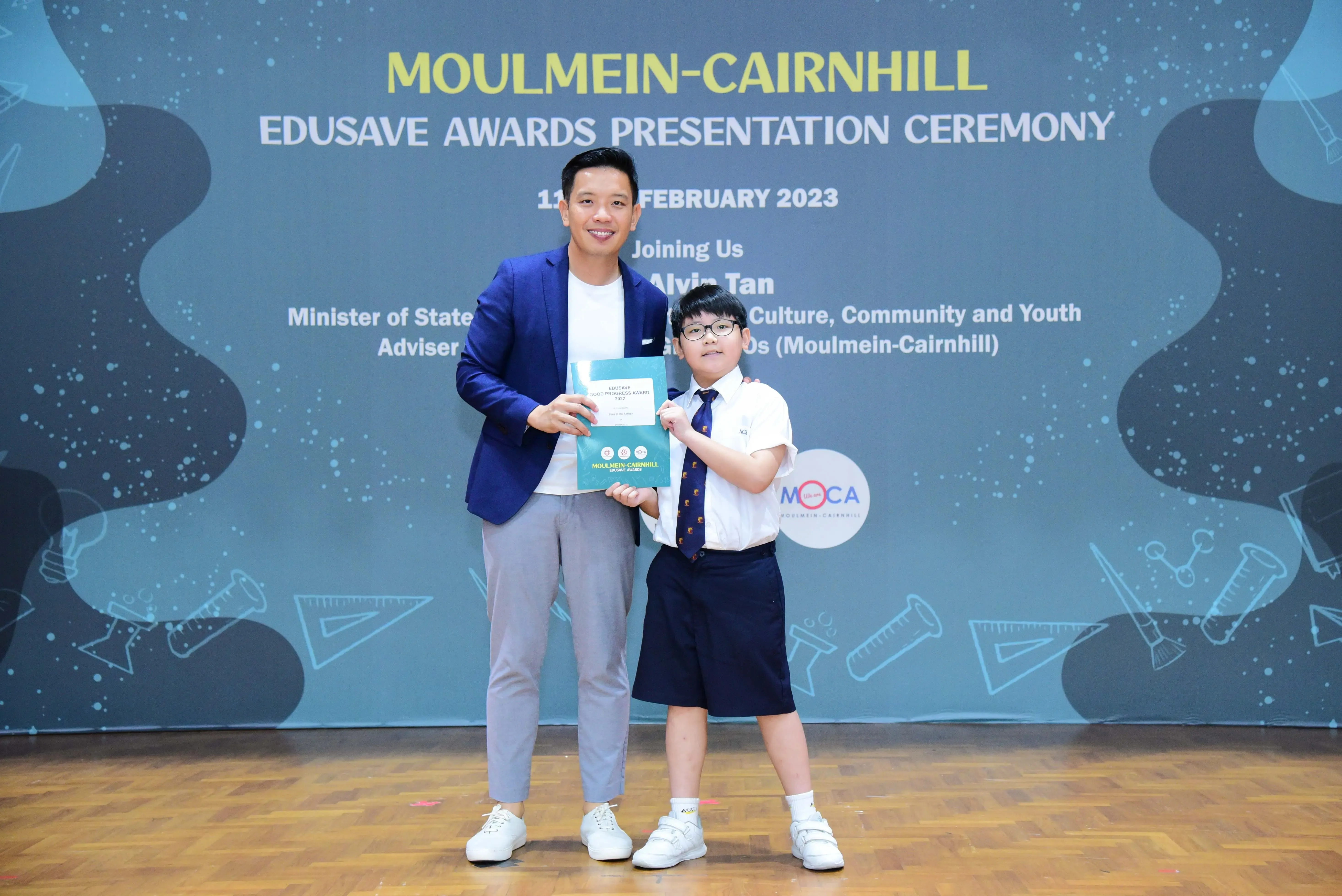 Adult in blue blazer and young student in uniform pose at Moulmein-Cairnhill Edusave Awards Ceremony, February 2023.