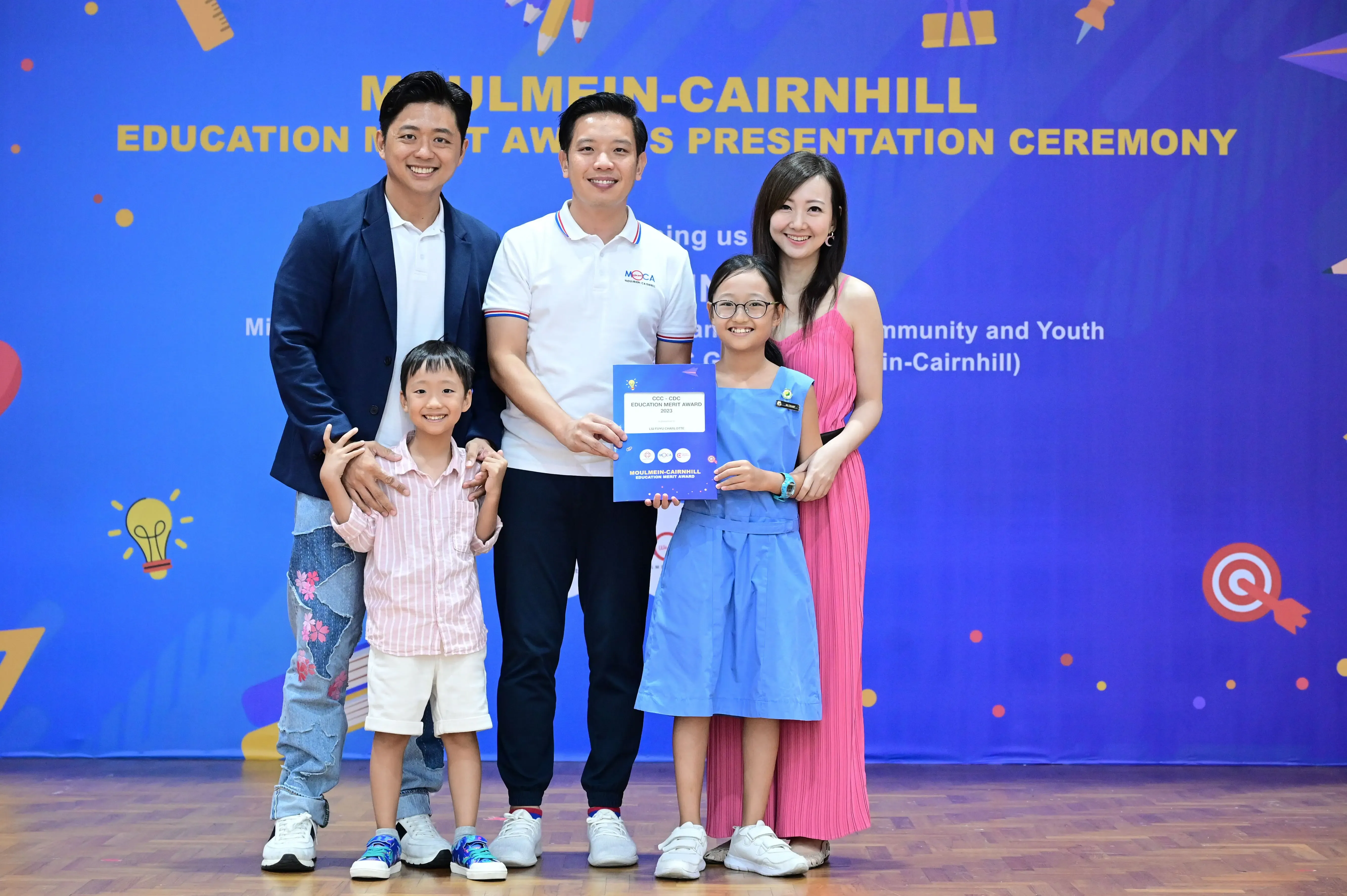 Five people pose at the Moulmein-Cairnhill Education Merit Awards Presentation Ceremony, with a girl holding a certificate.