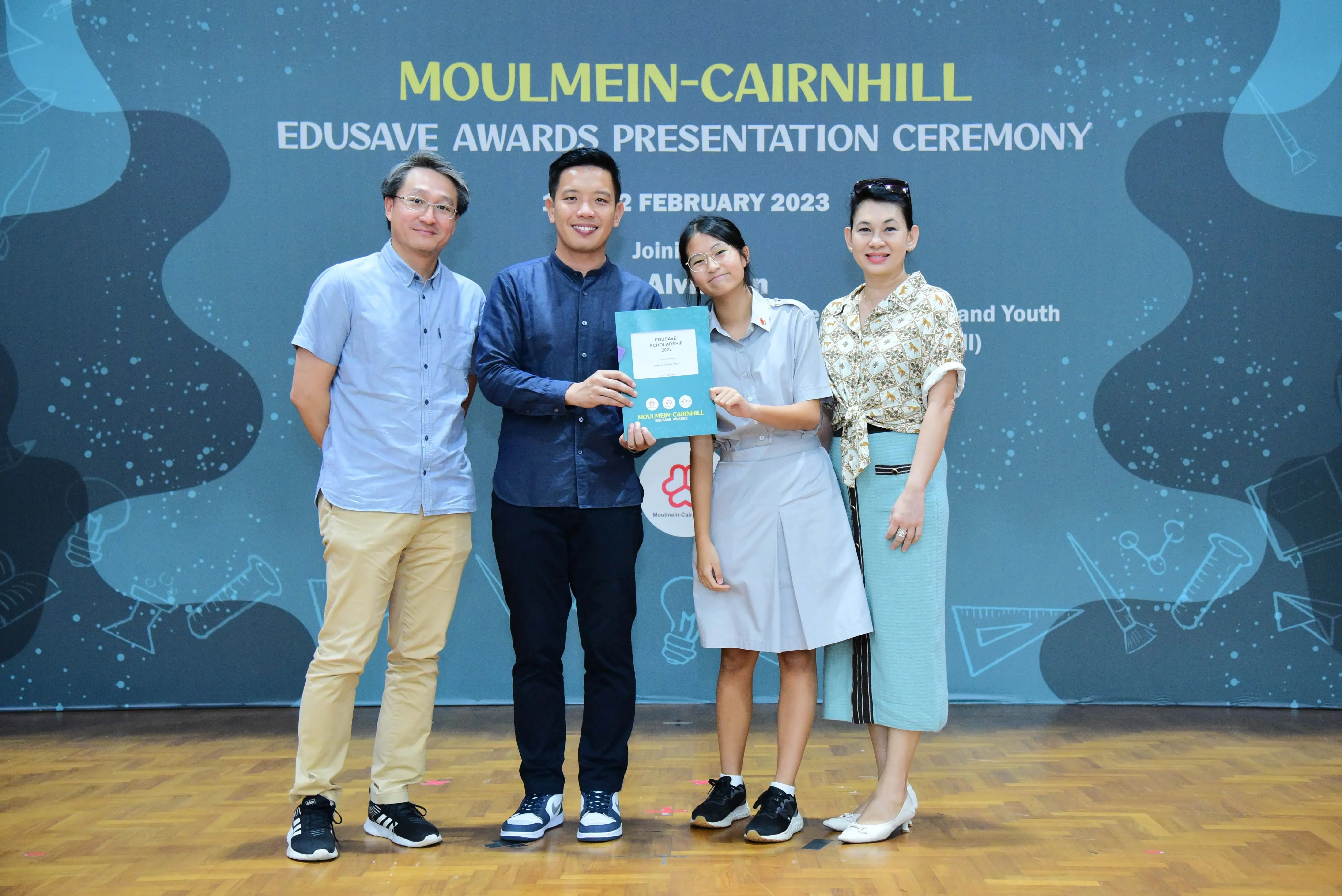 Four people pose on stage at the Moulmein-Cairnhill Edusave Awards Presentation Ceremony in February 2023.