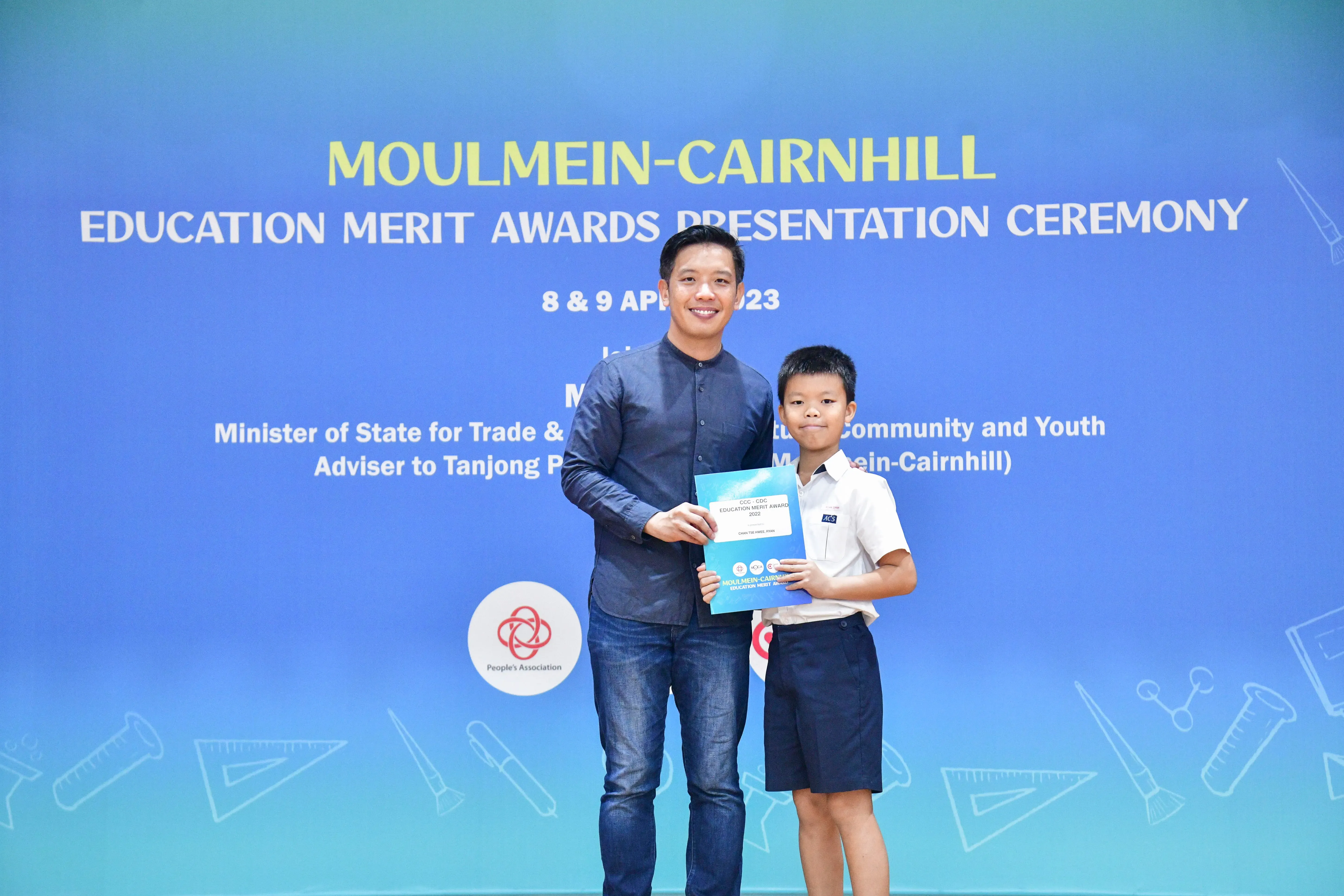 A man and a young boy hold a certificate together at the Moulmein-Cairnhill Education Merit Awards Ceremony.