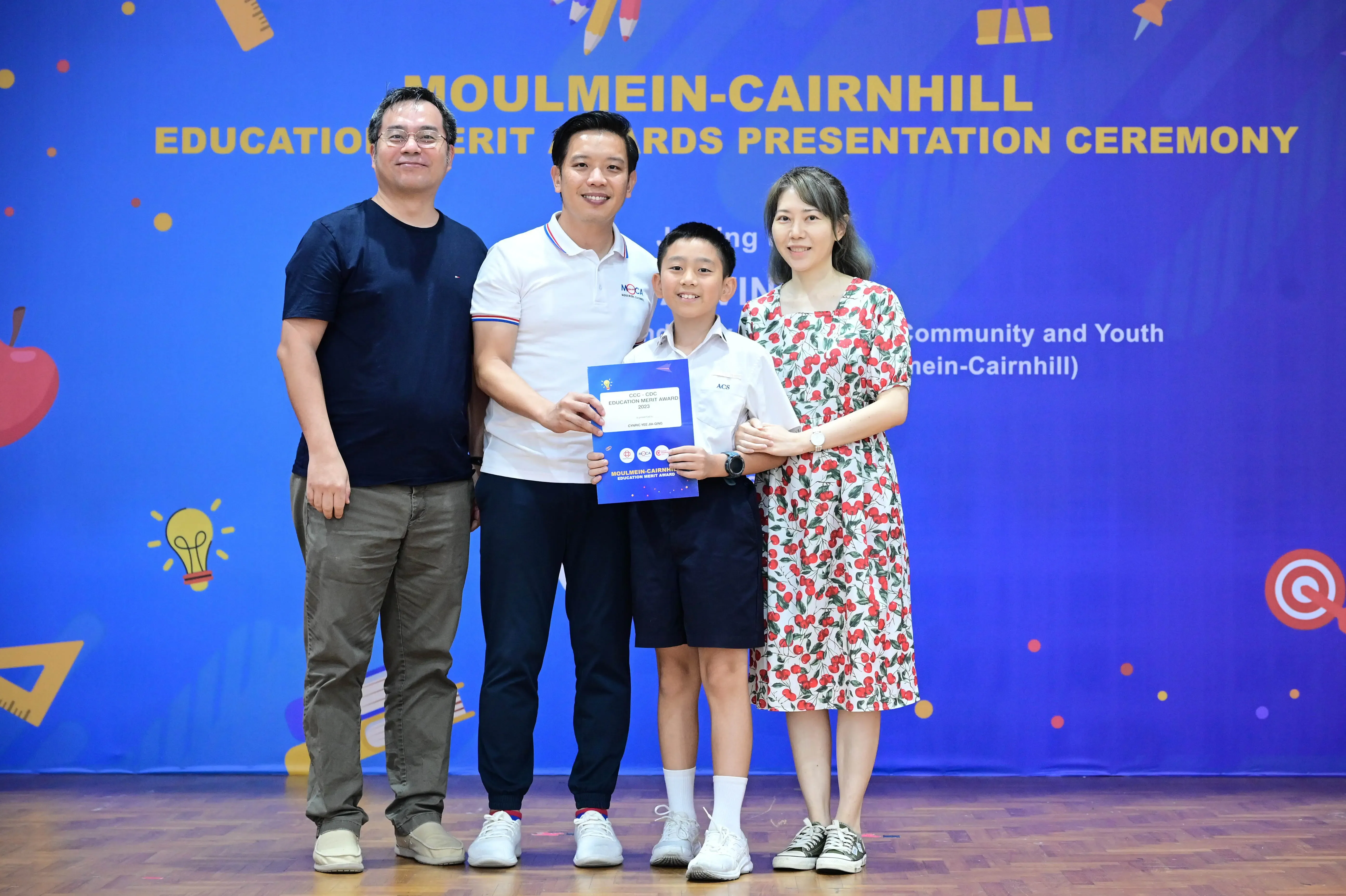 Three adults and a boy holding a certificate at the Moulmein-Cairnhill Education Merit Awards Presentation Ceremony.