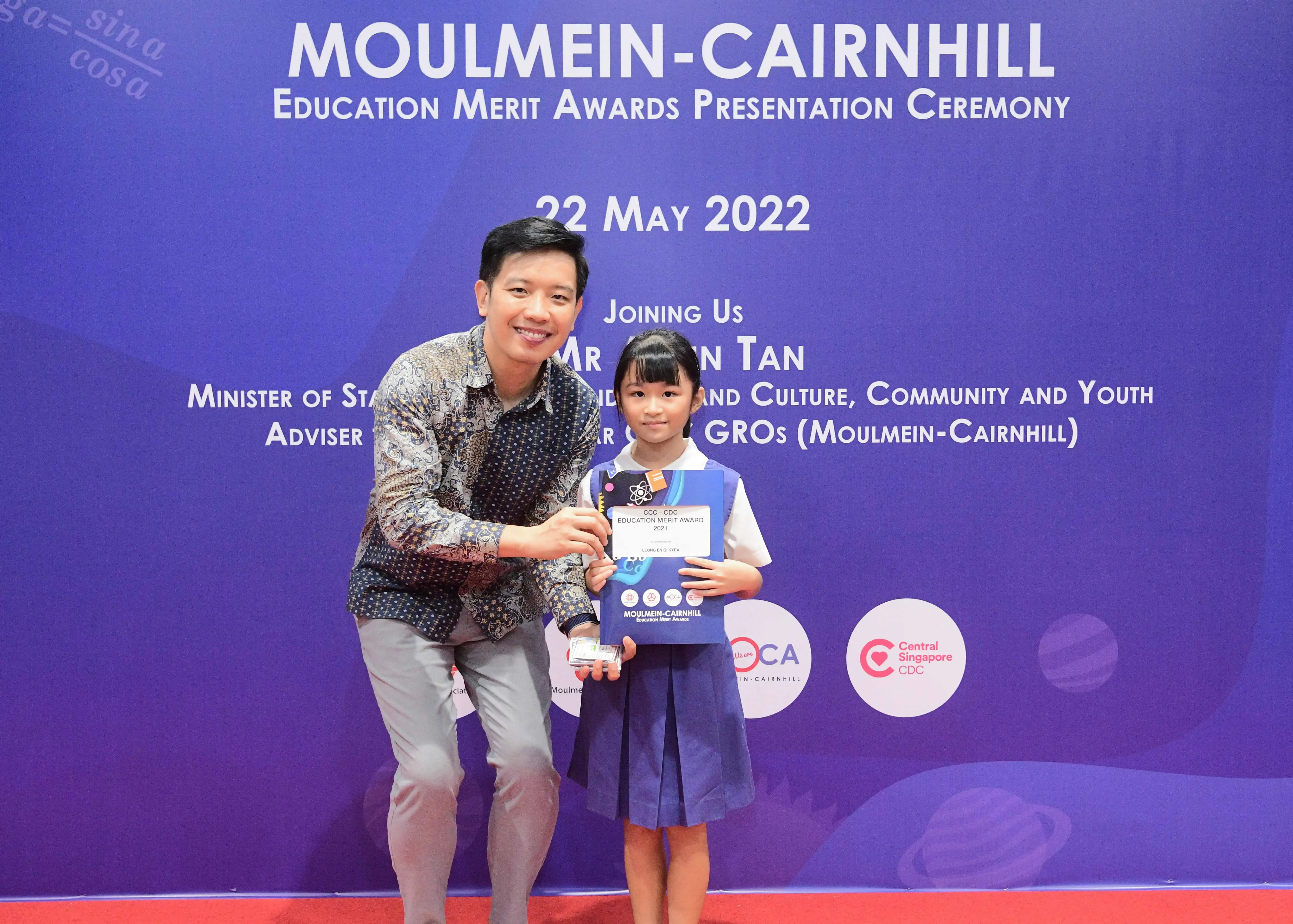 A man and a young girl pose together holding an award at the Moulmein-Cairnhill Education Merit Awards ceremony on 22 May 2022.