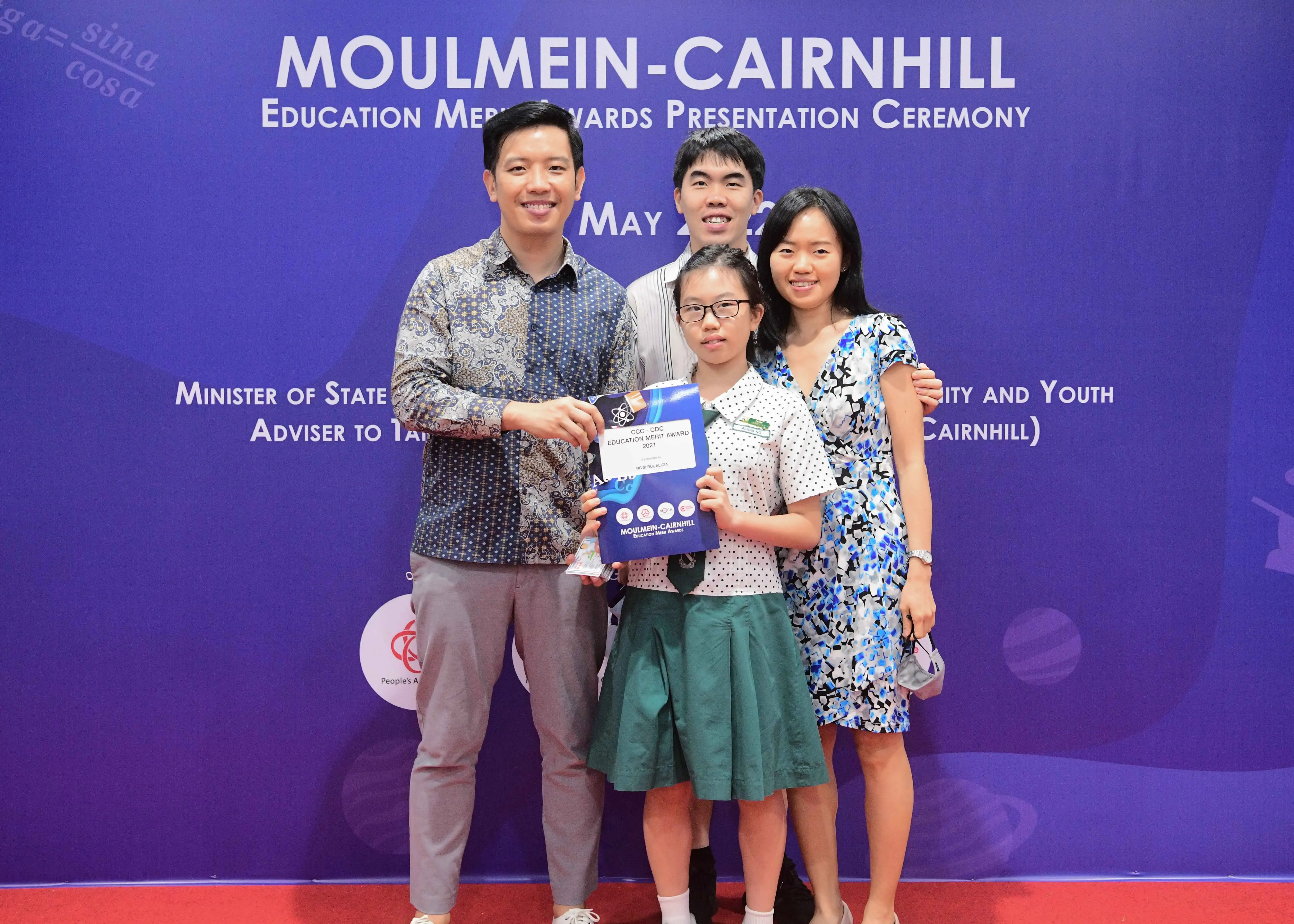 Four people pose together at the Moulmein-Cairnhill Education Merit Awards Presentation Ceremony, girl holding award.