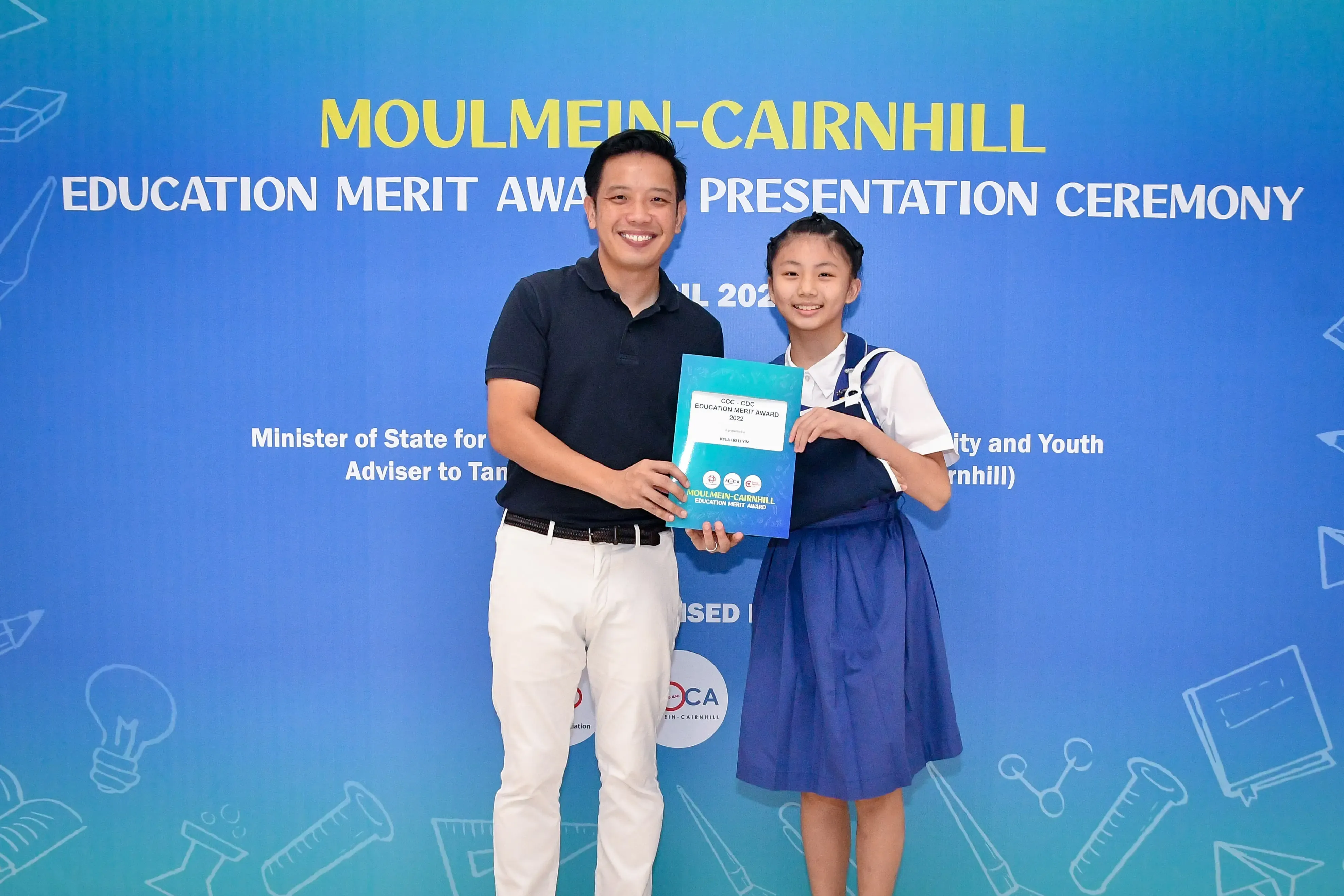 A man and a young girl hold an award certificate at the Moulmein-Cairnhill Education Merit Award Presentation Ceremony.