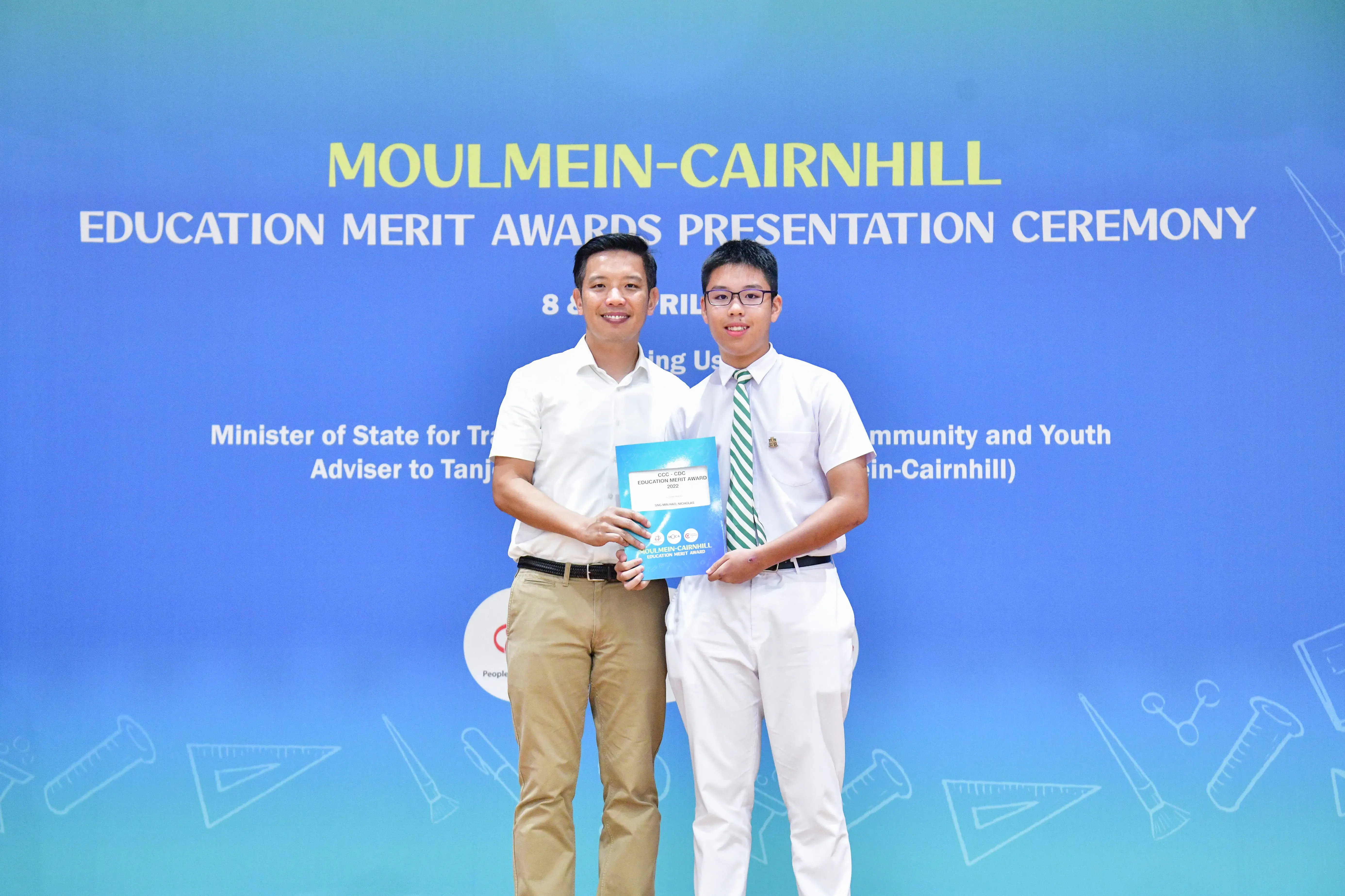 Two men pose holding an award booklet at the Moulmein-Cairnhill Education Merit Awards Presentation Ceremony.