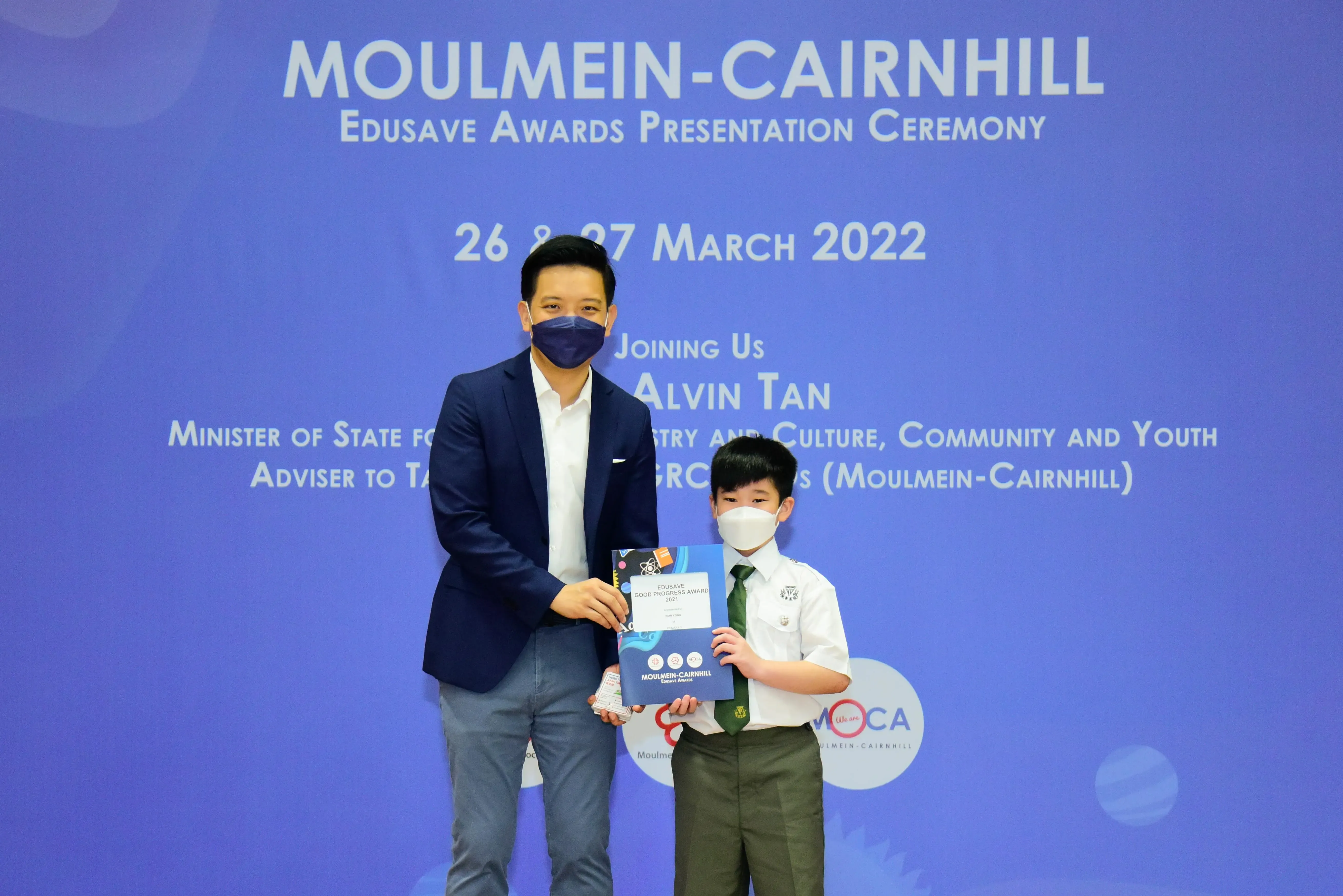 An adult and a young student in uniform hold an award at the Moulmein-Cairnhill Edusave Awards Ceremony, March 2022.