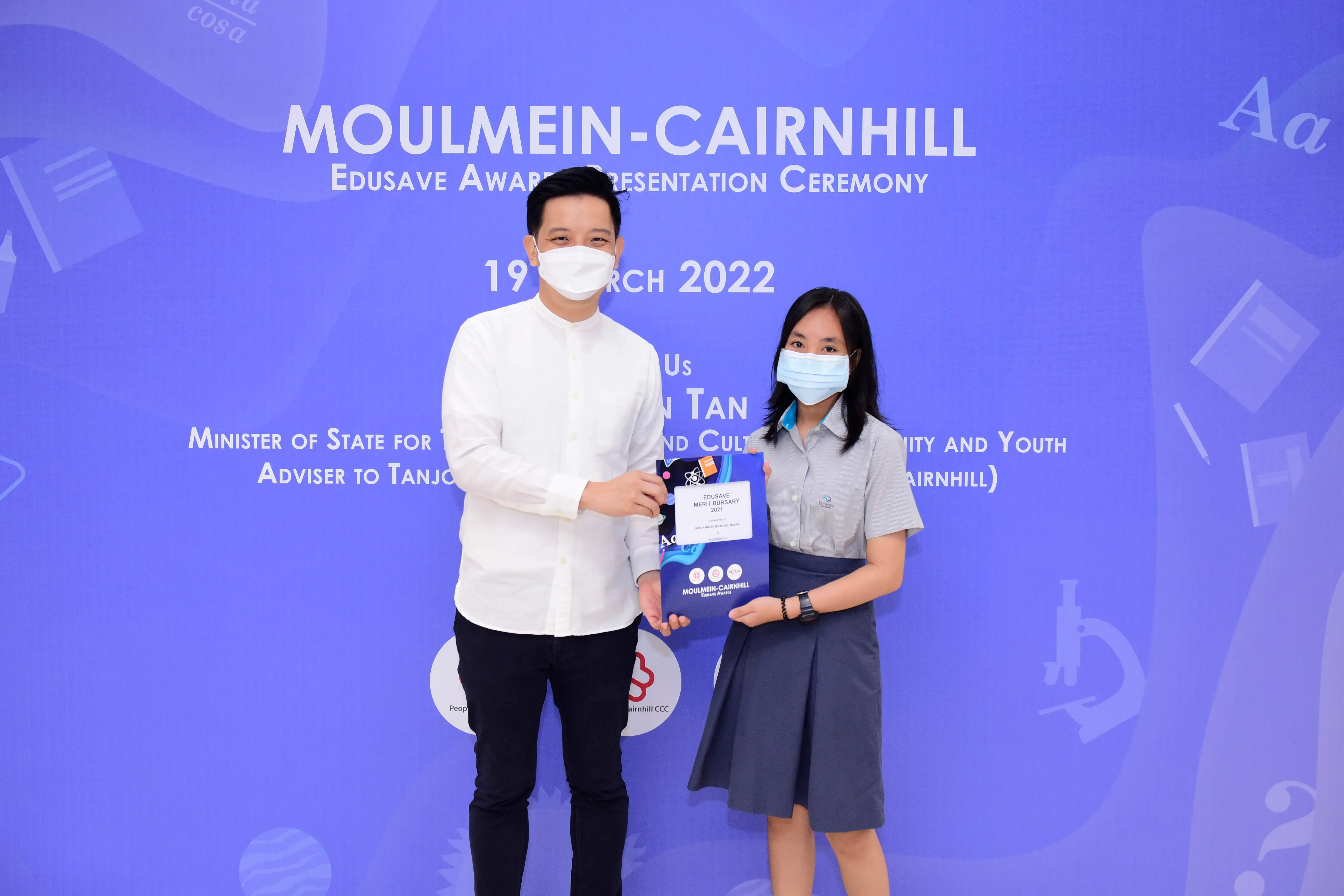 Two masked individuals hold an award certificate at the Moulmein-Cairnhill Edusave Award Ceremony on 19 March 2022.