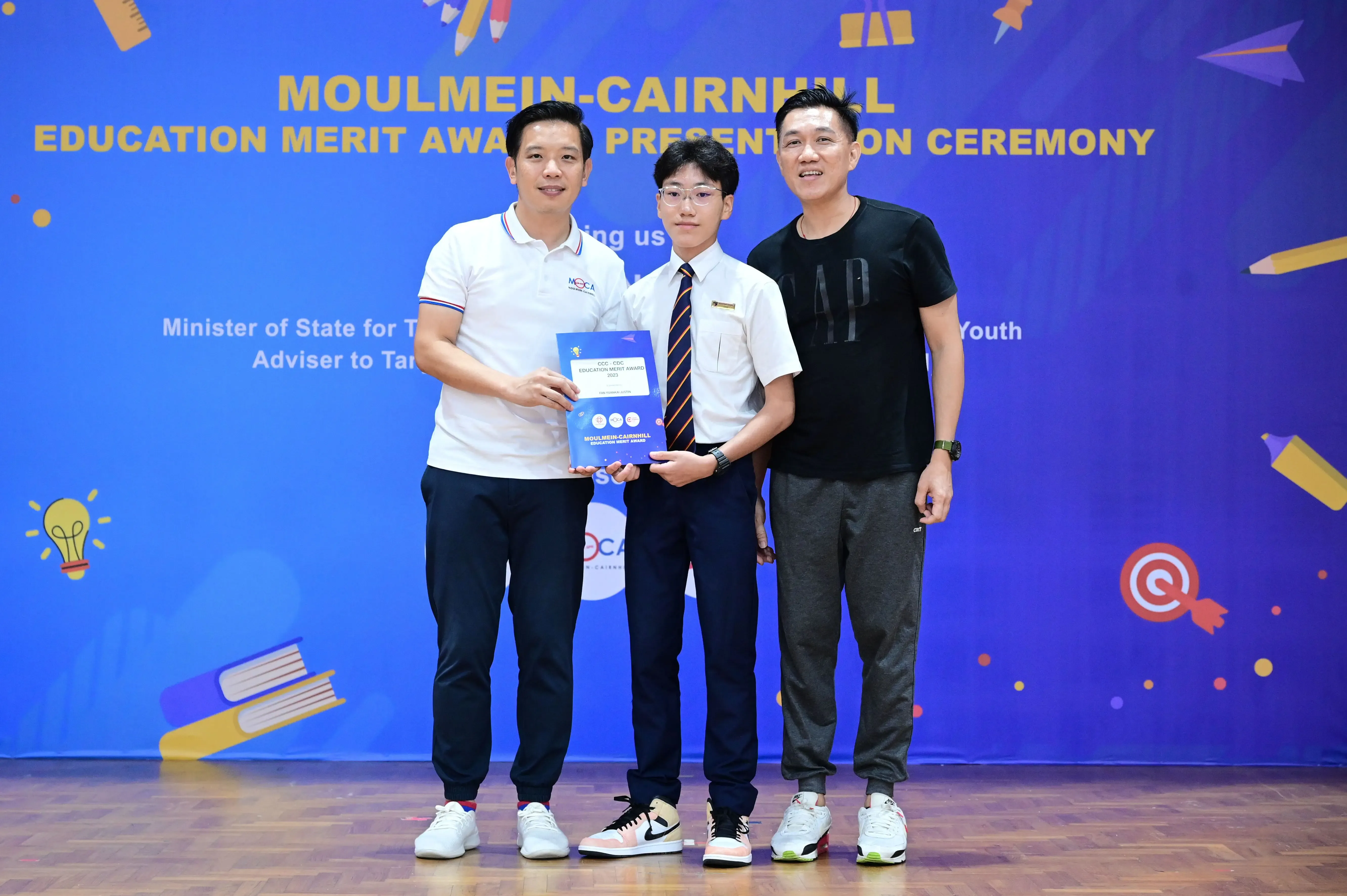 Three men pose together at the Moulmein-Cairnhill Education Merit Award Presentation Ceremony, holding a certificate.