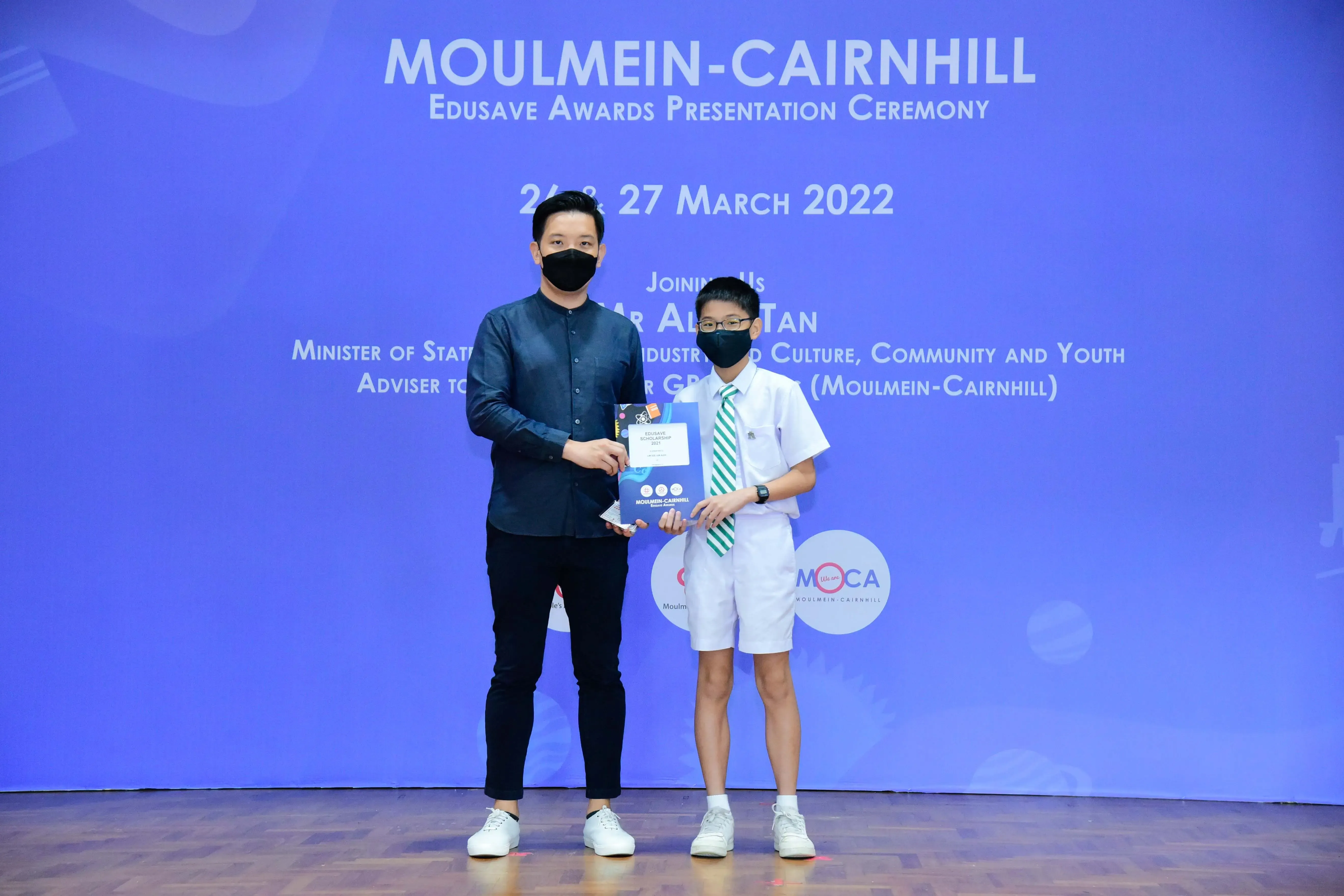 An adult and a young student in school uniform hold an award certificate at the Moulmein-Cairnhill Edusave Awards Ceremony 2022.