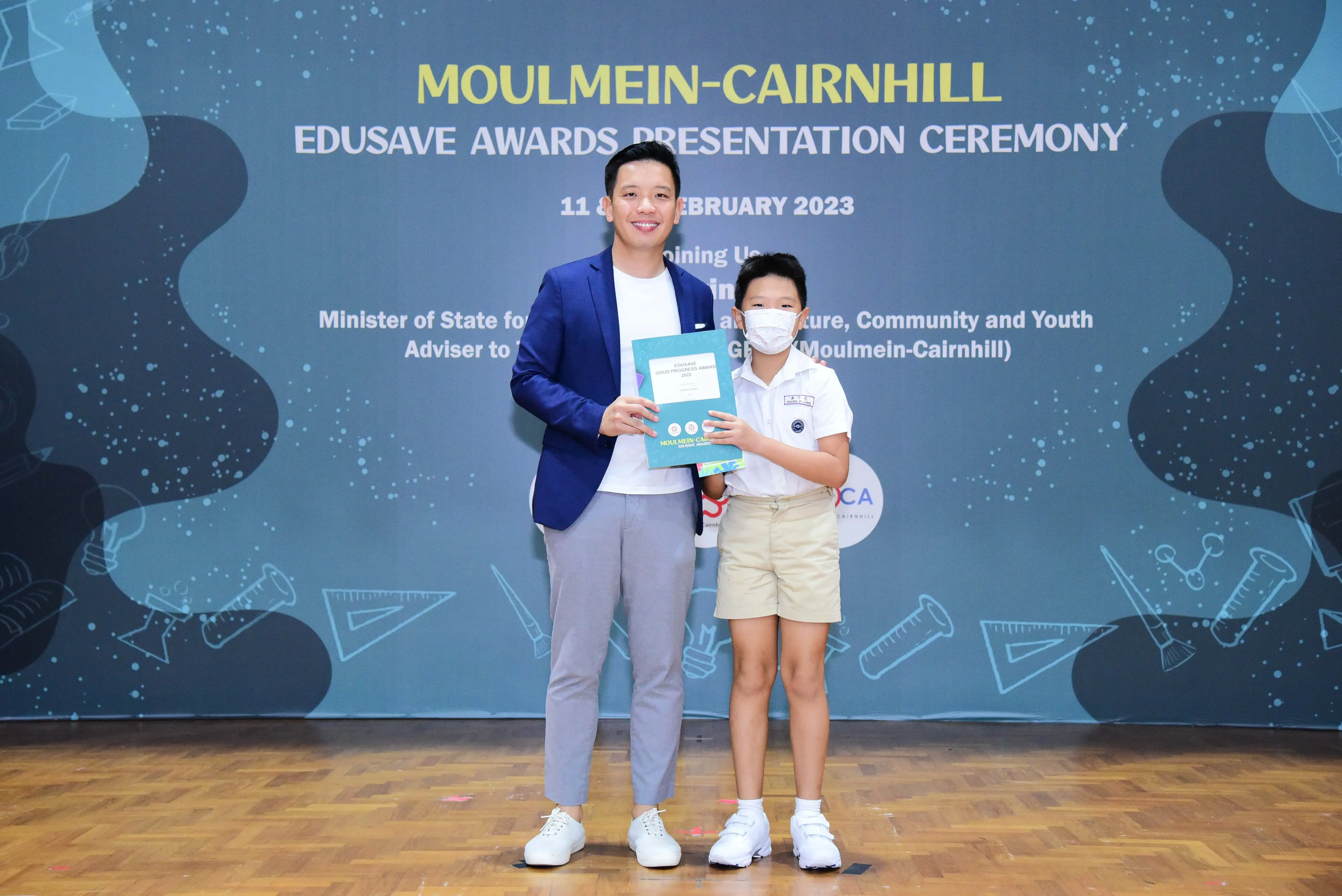 Man in blue blazer and young student holding an award at the Moulmein-Cairnhill Edusave Awards Ceremony 2023.
