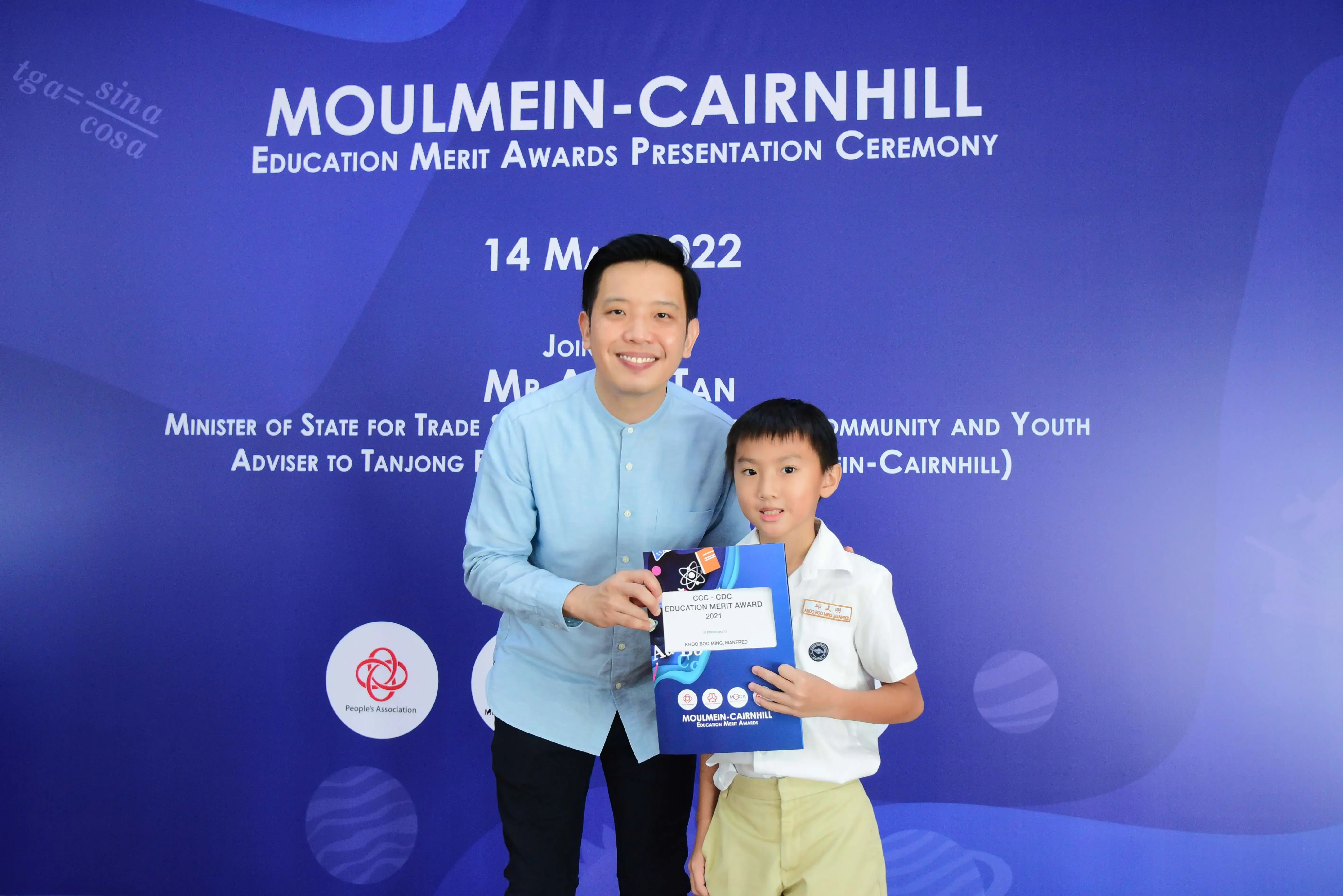 Man and young boy hold an award certificate at the Moulmein-Cairnhill Education Merit Awards Ceremony, May 2022.