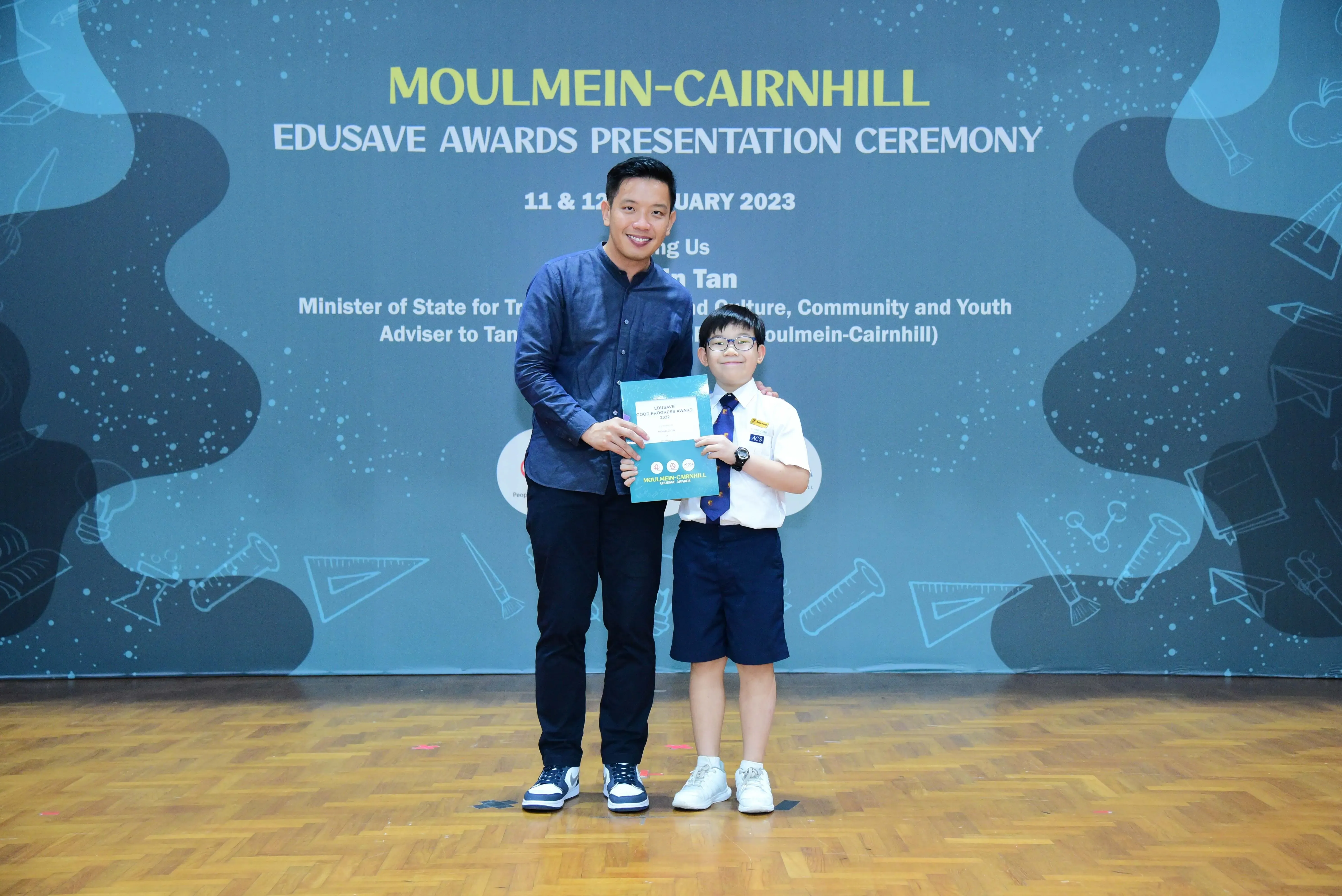 An adult and a young student hold a certificate at the Moulmein-Cairnhill Edusave Awards Presentation Ceremony 2023.