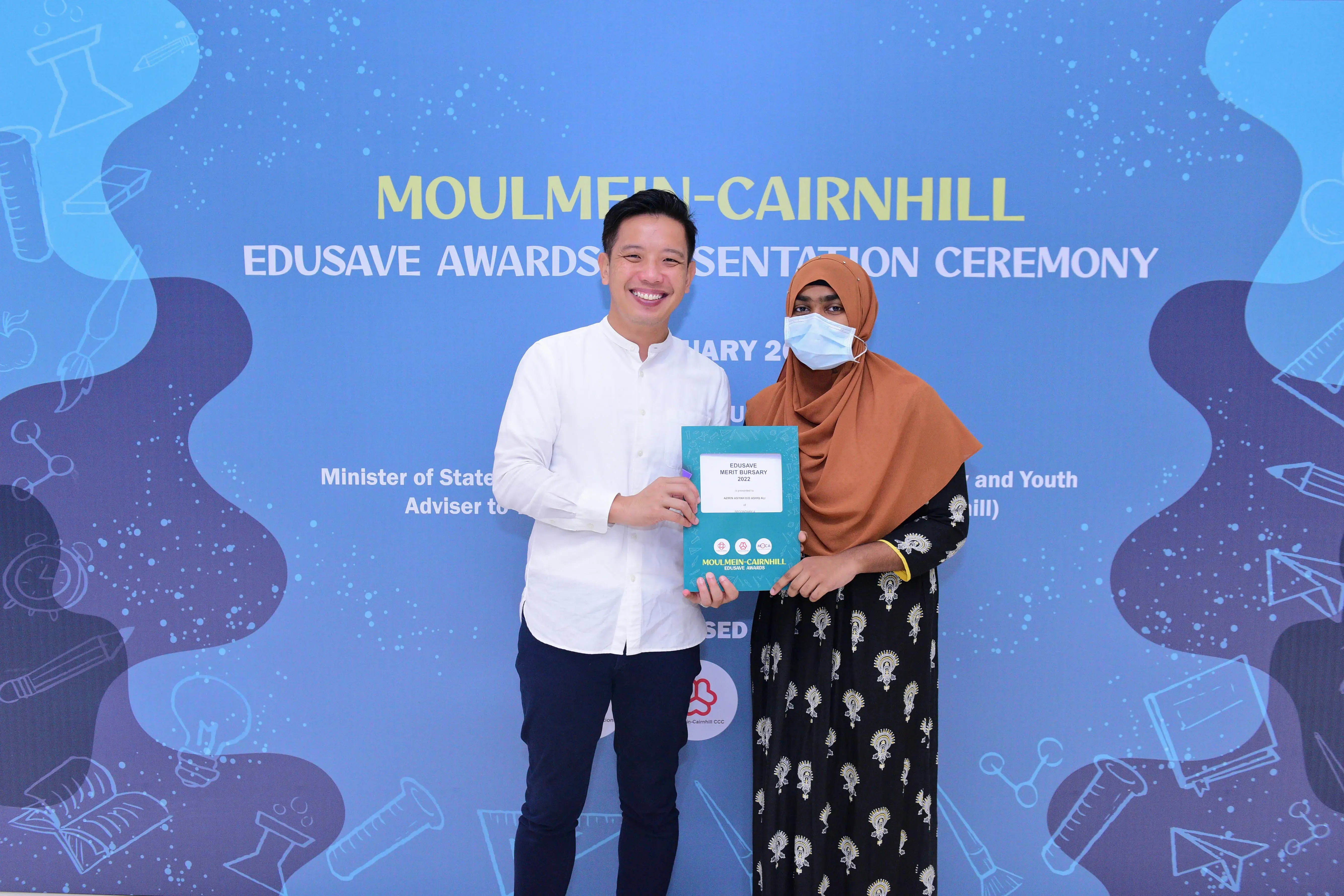 Two people hold a teal Edusave Merit Bursary certificate at the Moulmein-Cairnhill Awards Presentation Ceremony.