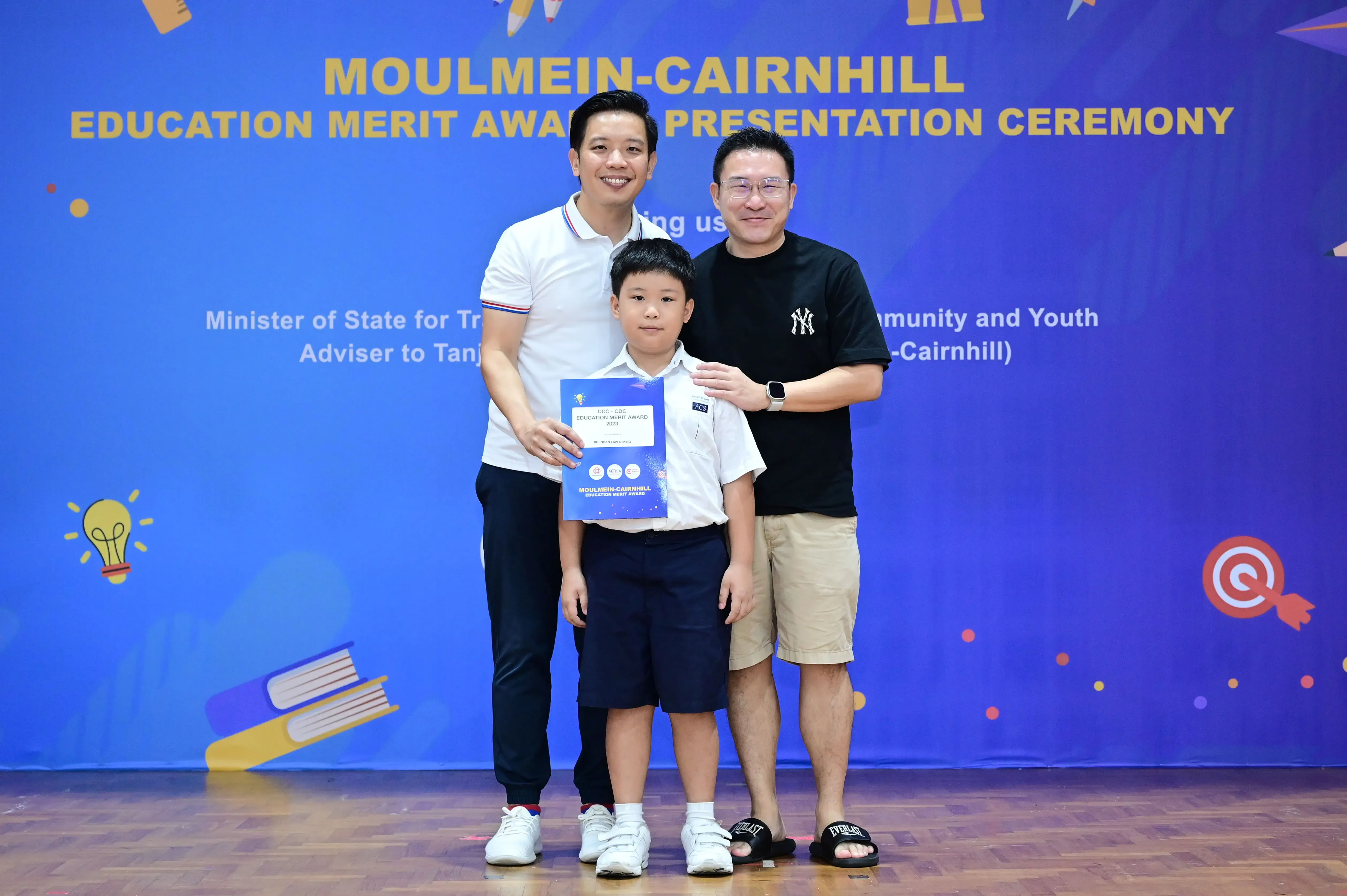 Two men and a boy pose at the Moulmein-Cairnhill Education Merit Award Presentation Ceremony, boy holding a certificate.