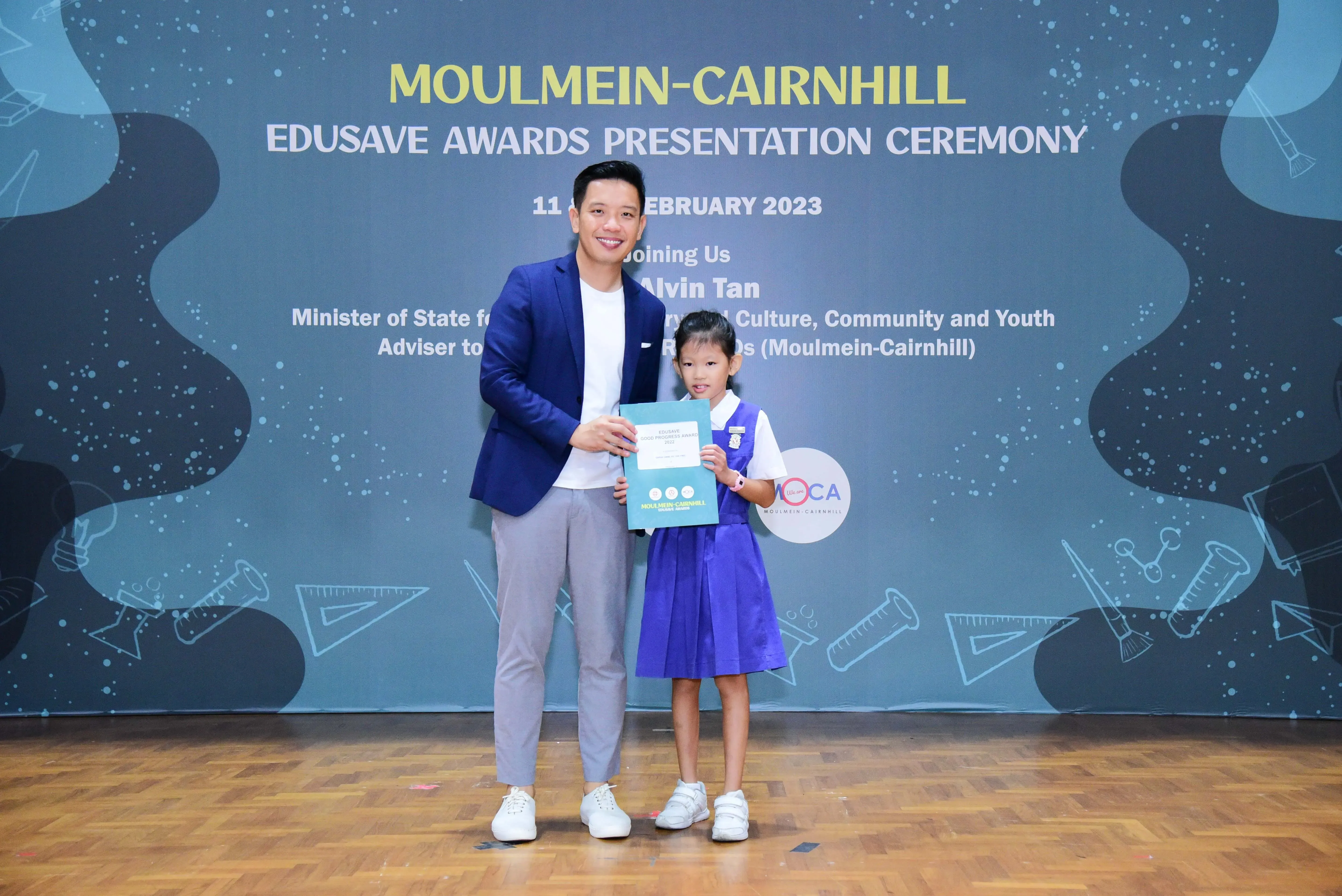 Man in blue blazer and young girl in school uniform hold a certificate at Moulmein-Cairnhill Edusave Awards 2023.