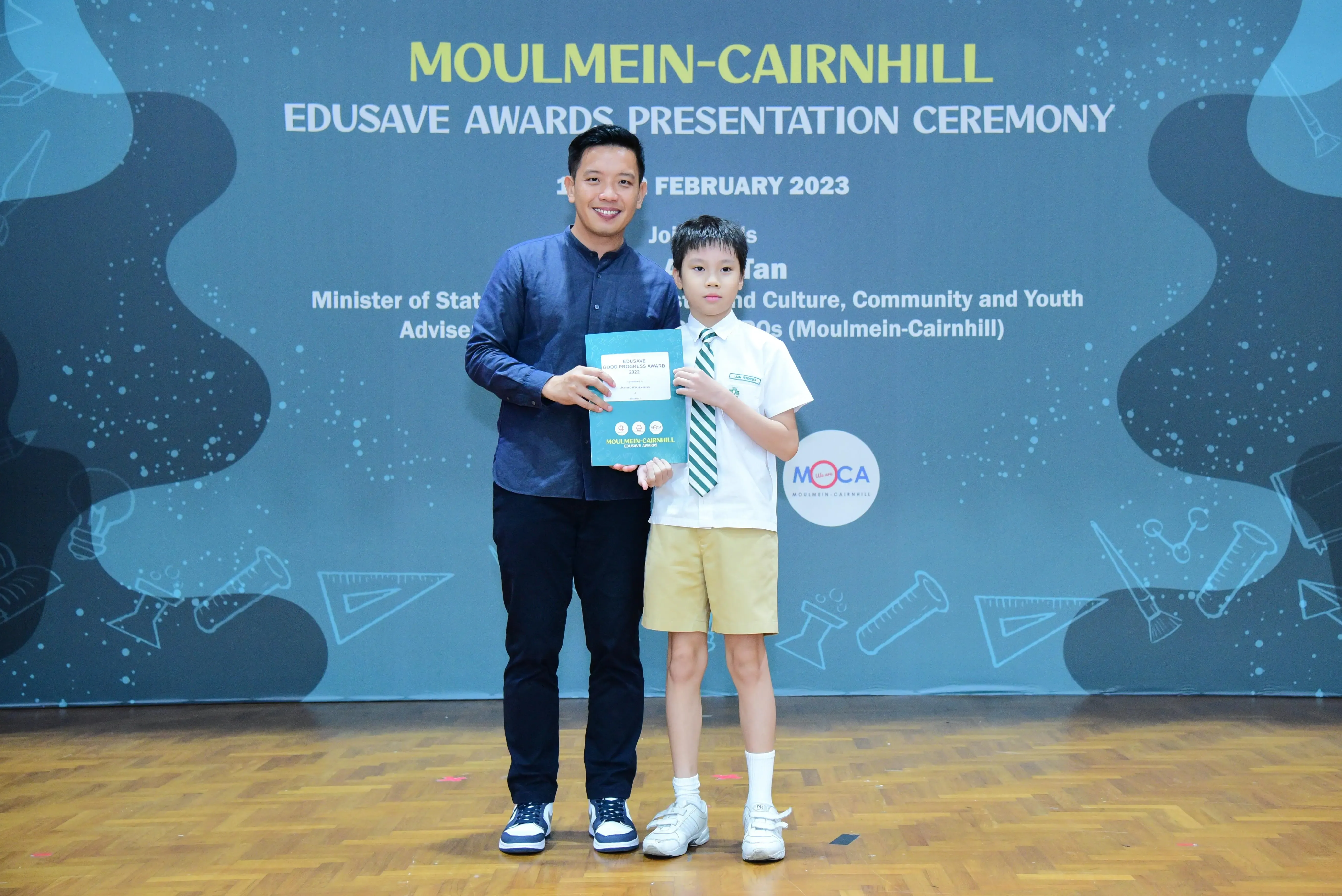 An adult and a young boy hold a certificate at the Moulmein-Cairnhill Edusave Awards Presentation Ceremony 2023.