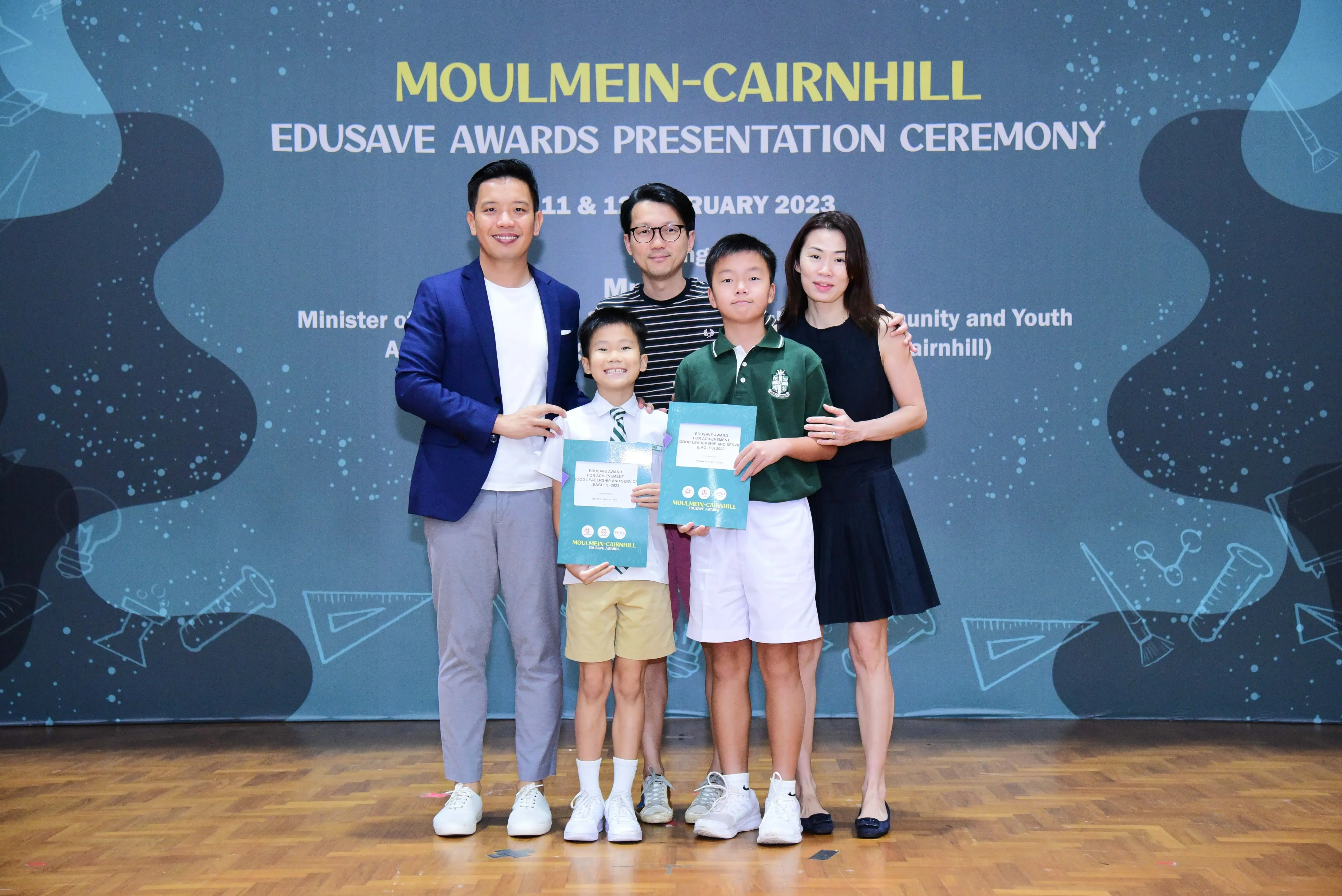 Five people pose at the Moulmein-Cairnhill Edusave Awards Presentation Ceremony, two boys holding award certificates.