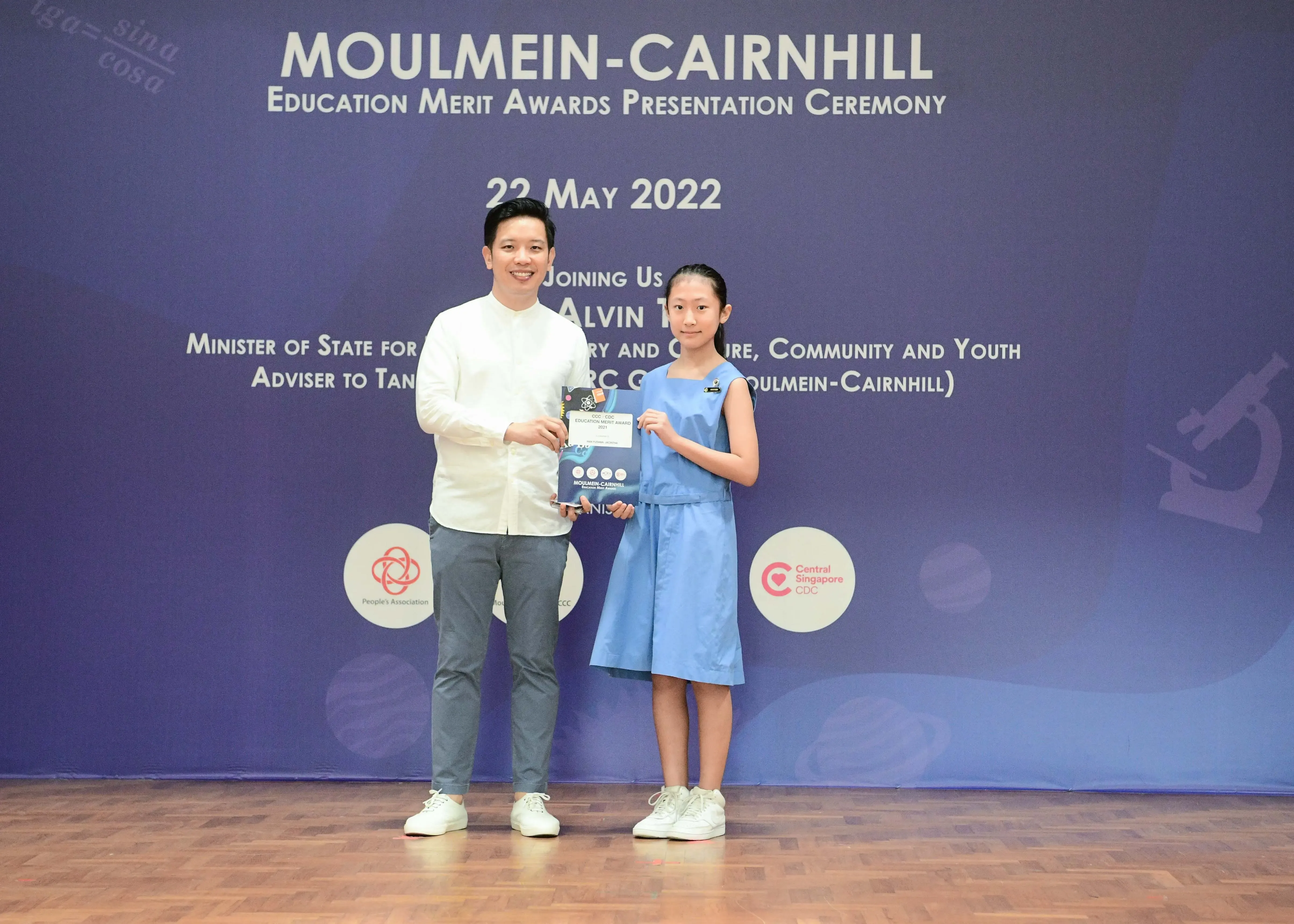 A man and a young girl hold an award booklet at the Moulmein-Cairnhill Education Merit Awards Ceremony on 22 May 2022.