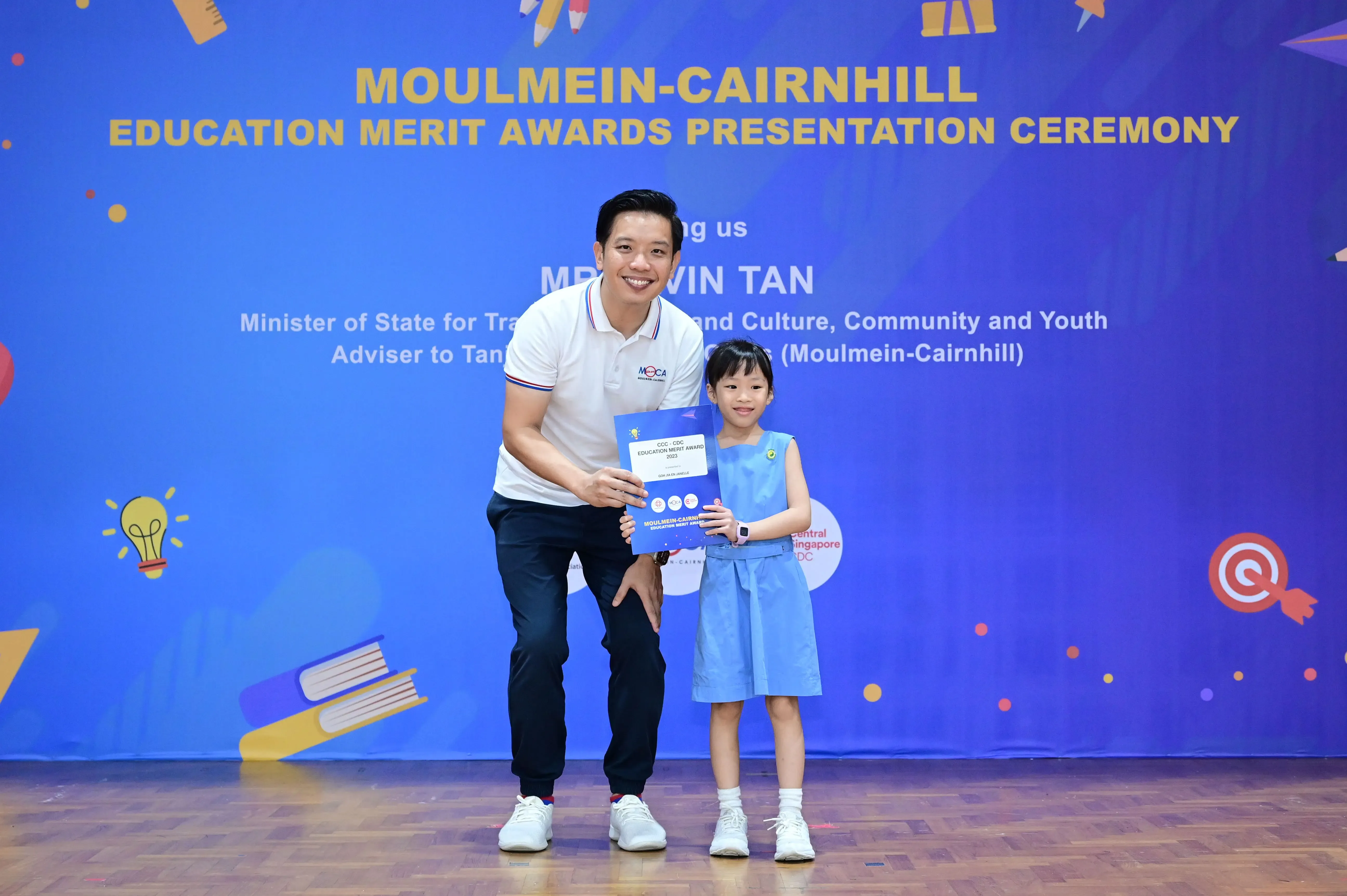 A man and a young girl hold a certificate at the Moulmein-Cairnhill Education Merit Awards Presentation Ceremony.