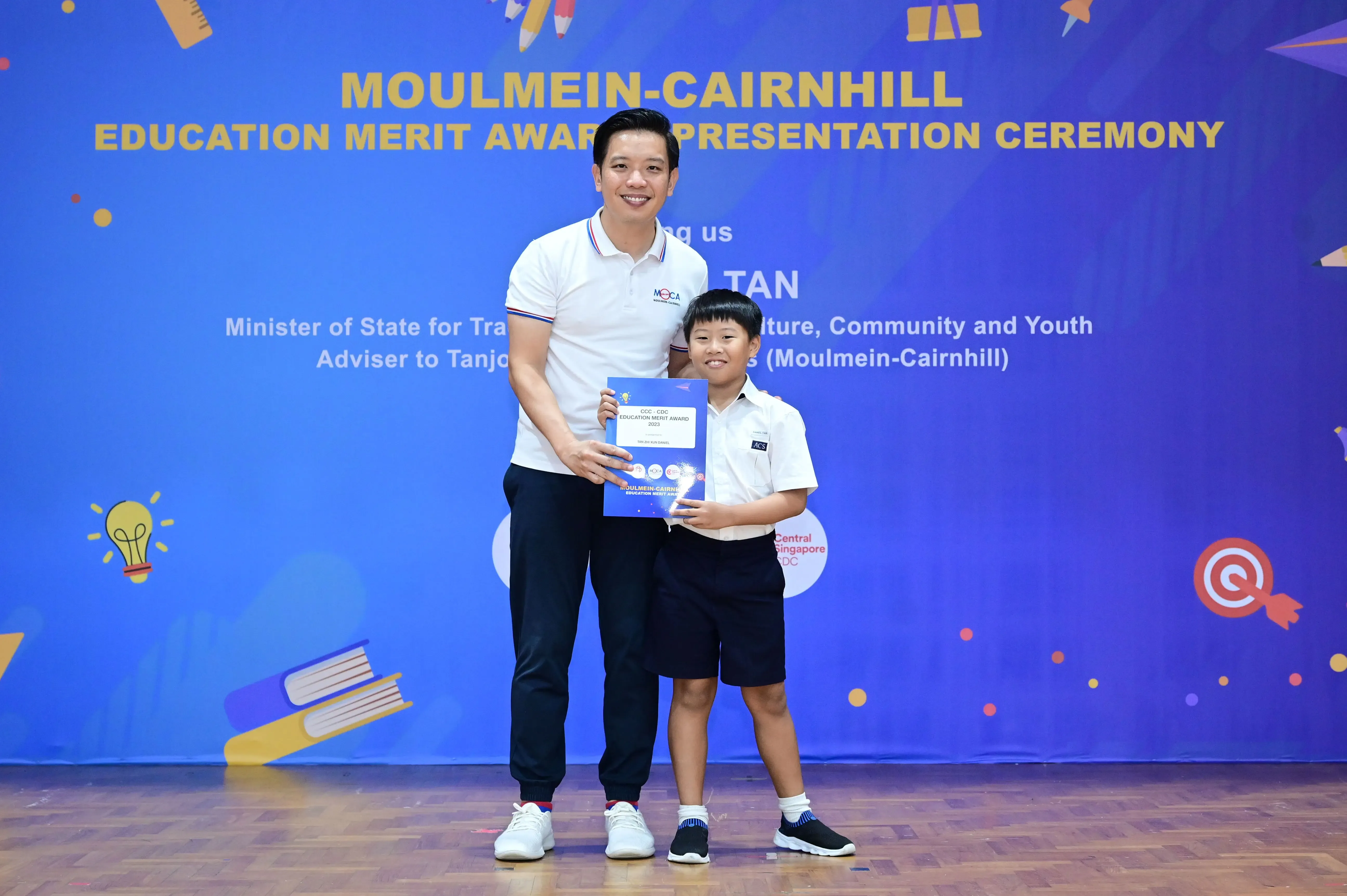 A man and a young boy hold an award certificate at the Moulmein-Cairnhill Education Merit Award Presentation Ceremony.