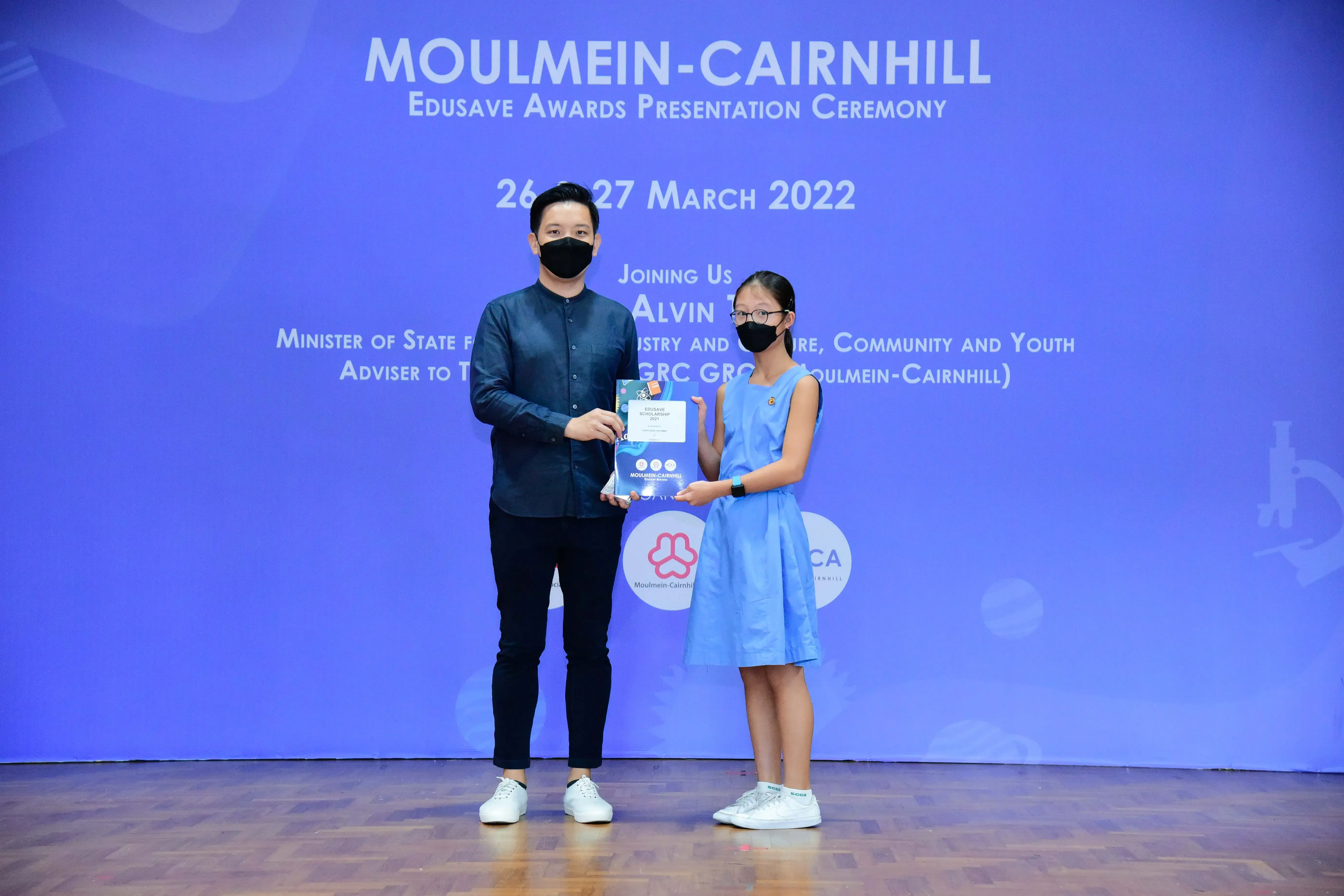 A man and a girl wearing masks hold a certificate at the Moulmein-Cairnhill Edusave Awards Ceremony, March 2022.