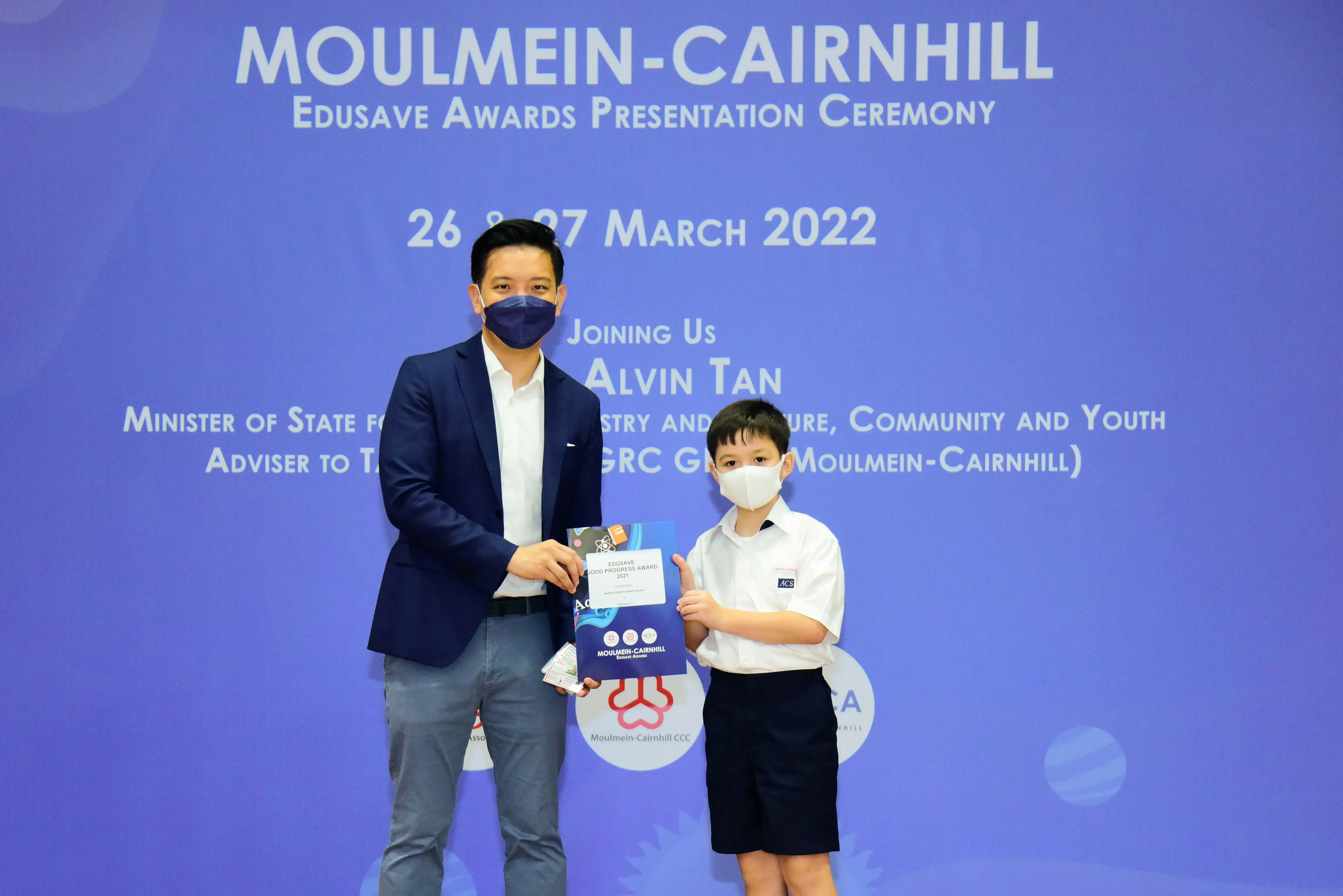 An adult and a young boy in masks hold an award at the Moulmein-Cairnhill Edusave Awards Ceremony, March 2022.