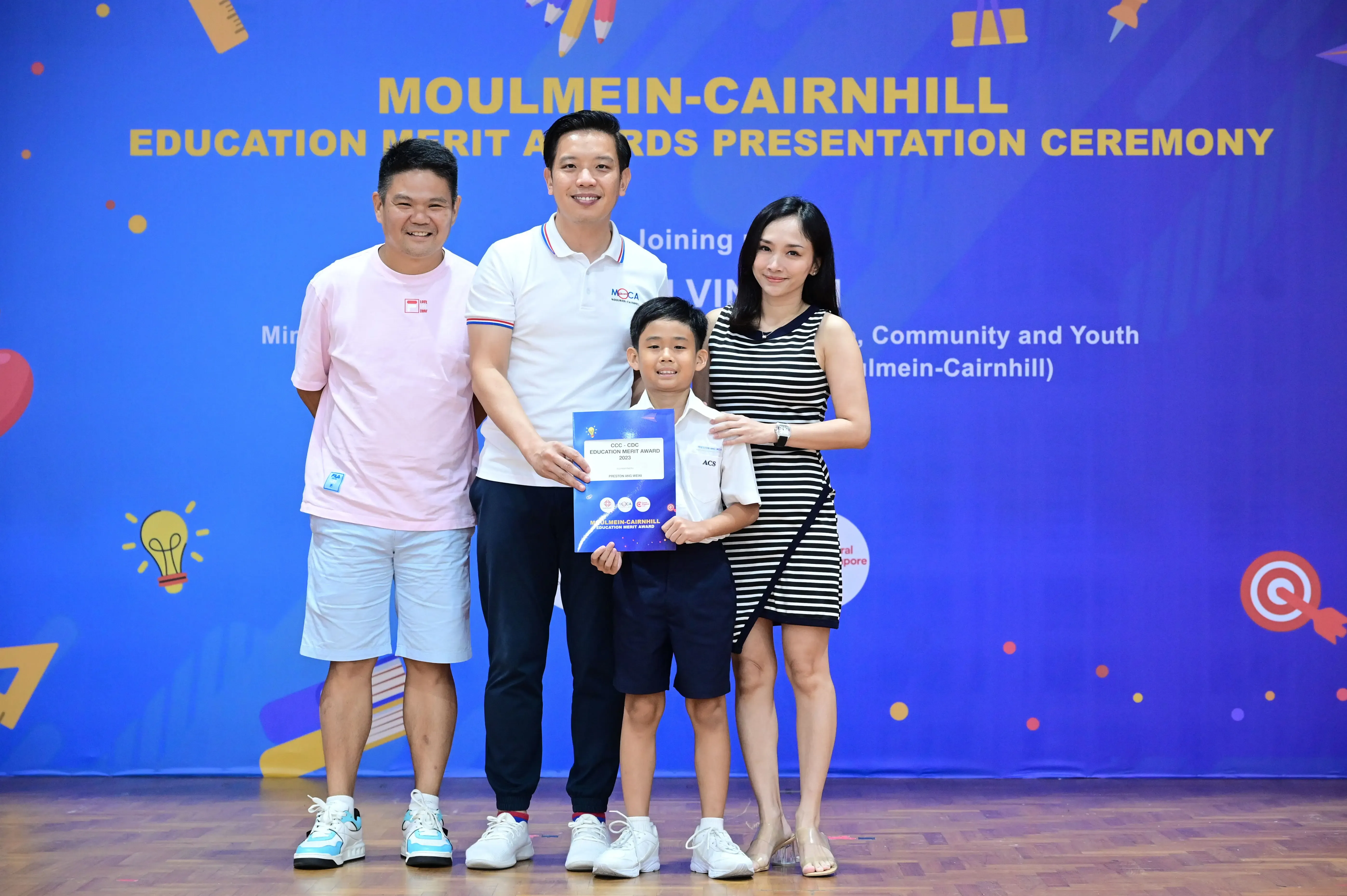 Three adults and a boy pose with an award certificate at the Moulmein-Cairnhill Education Merit Awards ceremony.