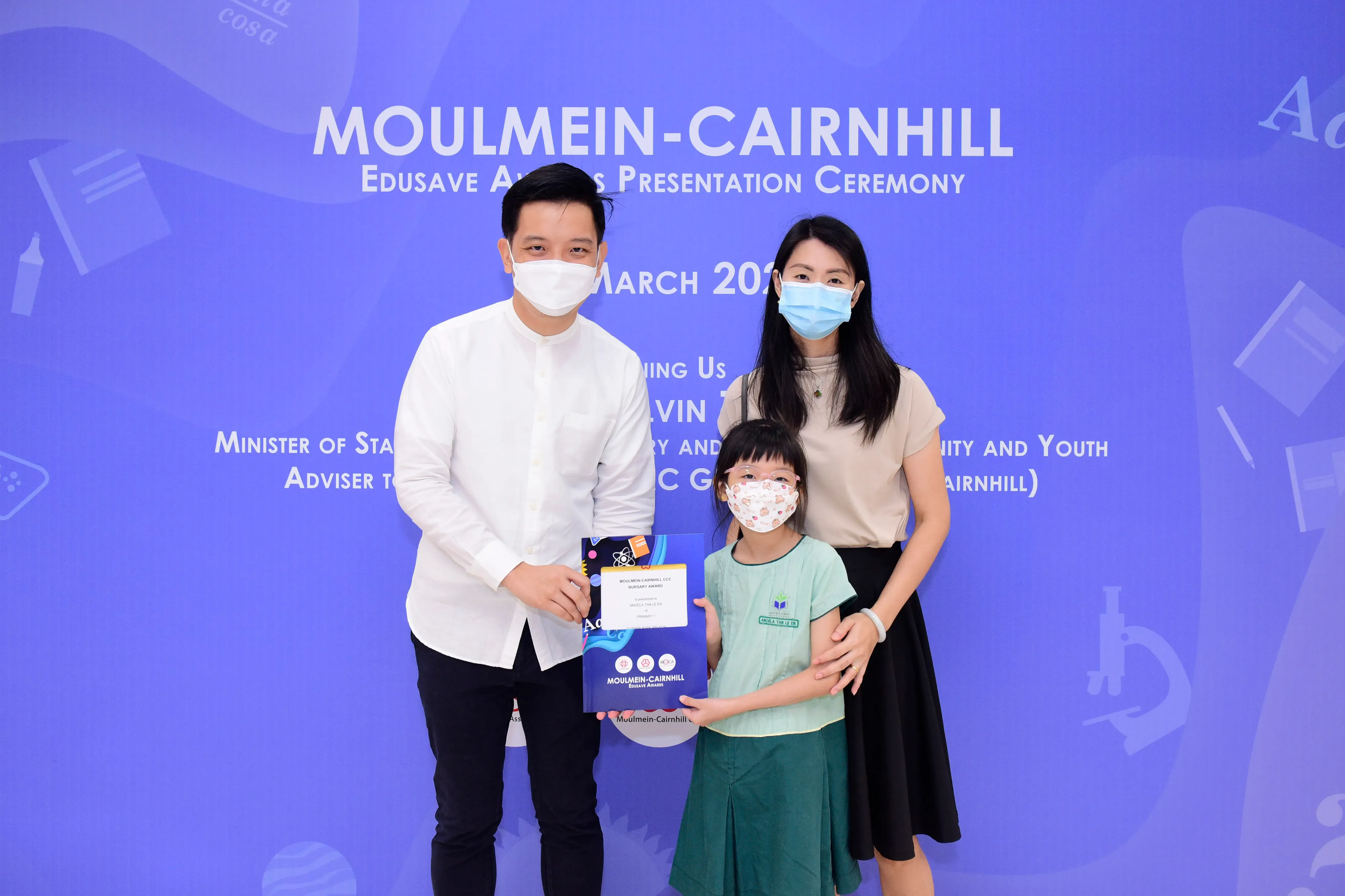 Two masked adults and a young girl holding an award certificate at the Moulmein-Cairnhill Edusave Awards Ceremony.