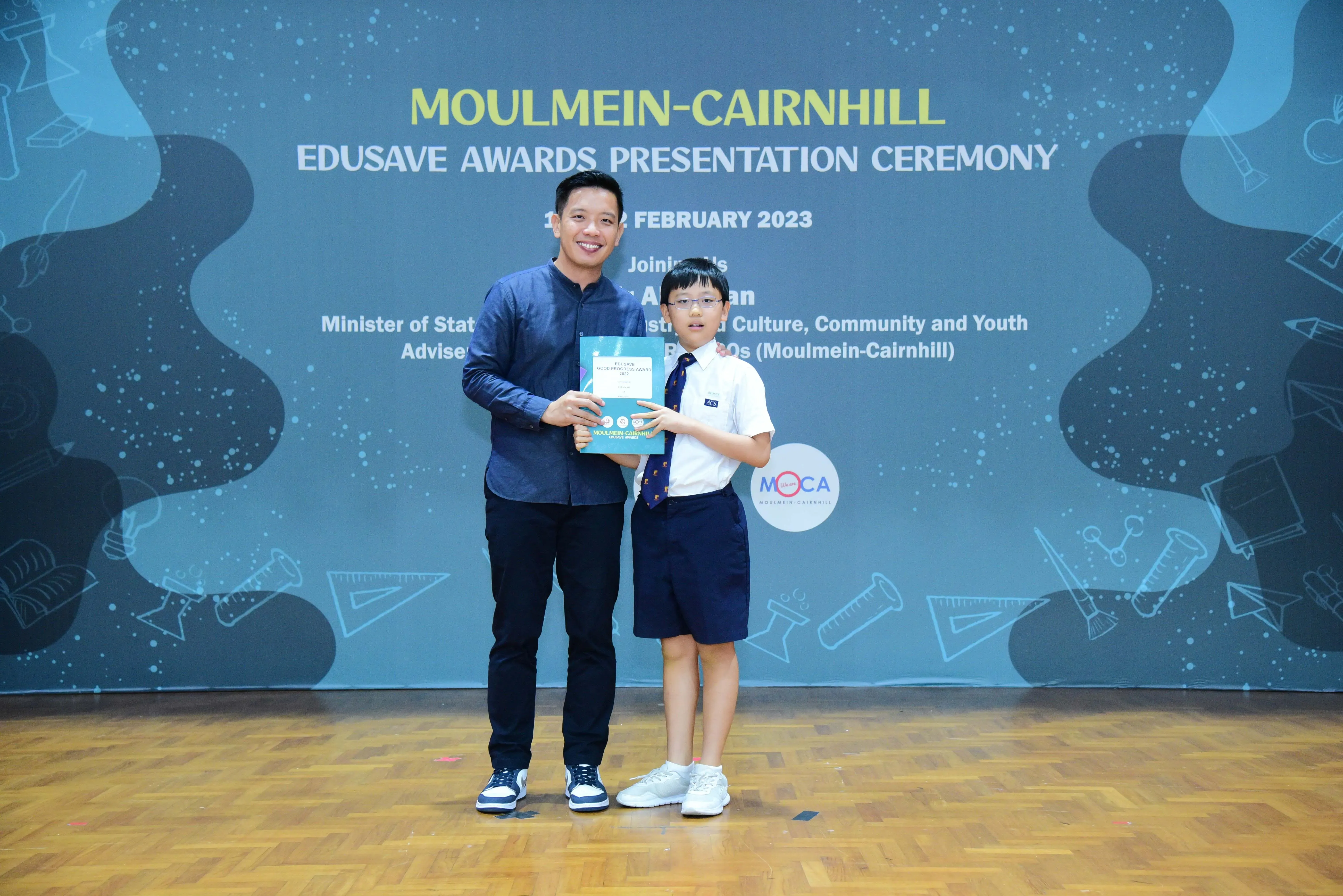 An adult and a uniformed student hold a certificate at the Moulmein-Cairnhill Edusave Awards Ceremony, February 2023.