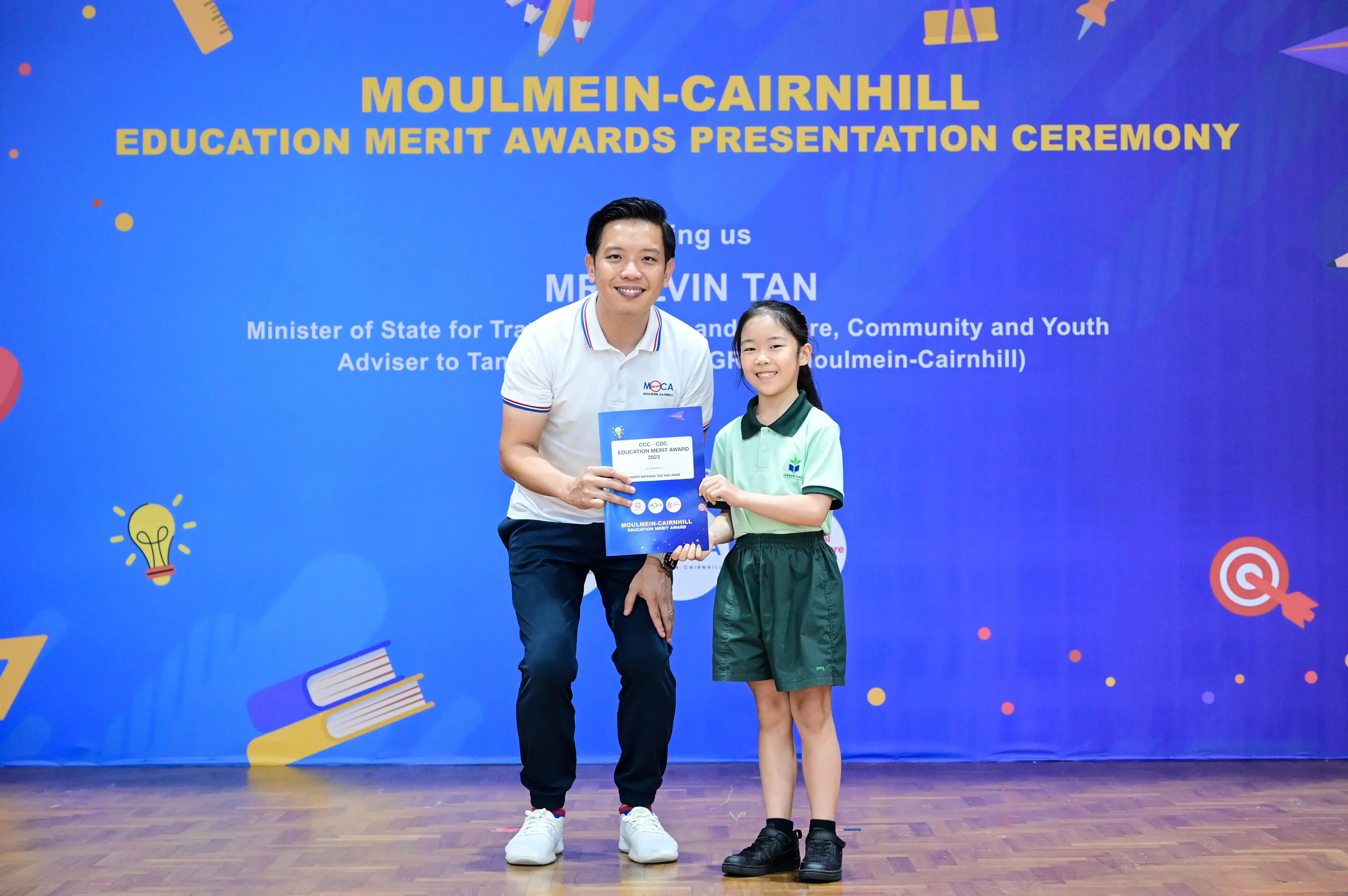 A man and a young girl in school uniform hold a certificate at the Moulmein-Cairnhill Education Merit Awards ceremony.