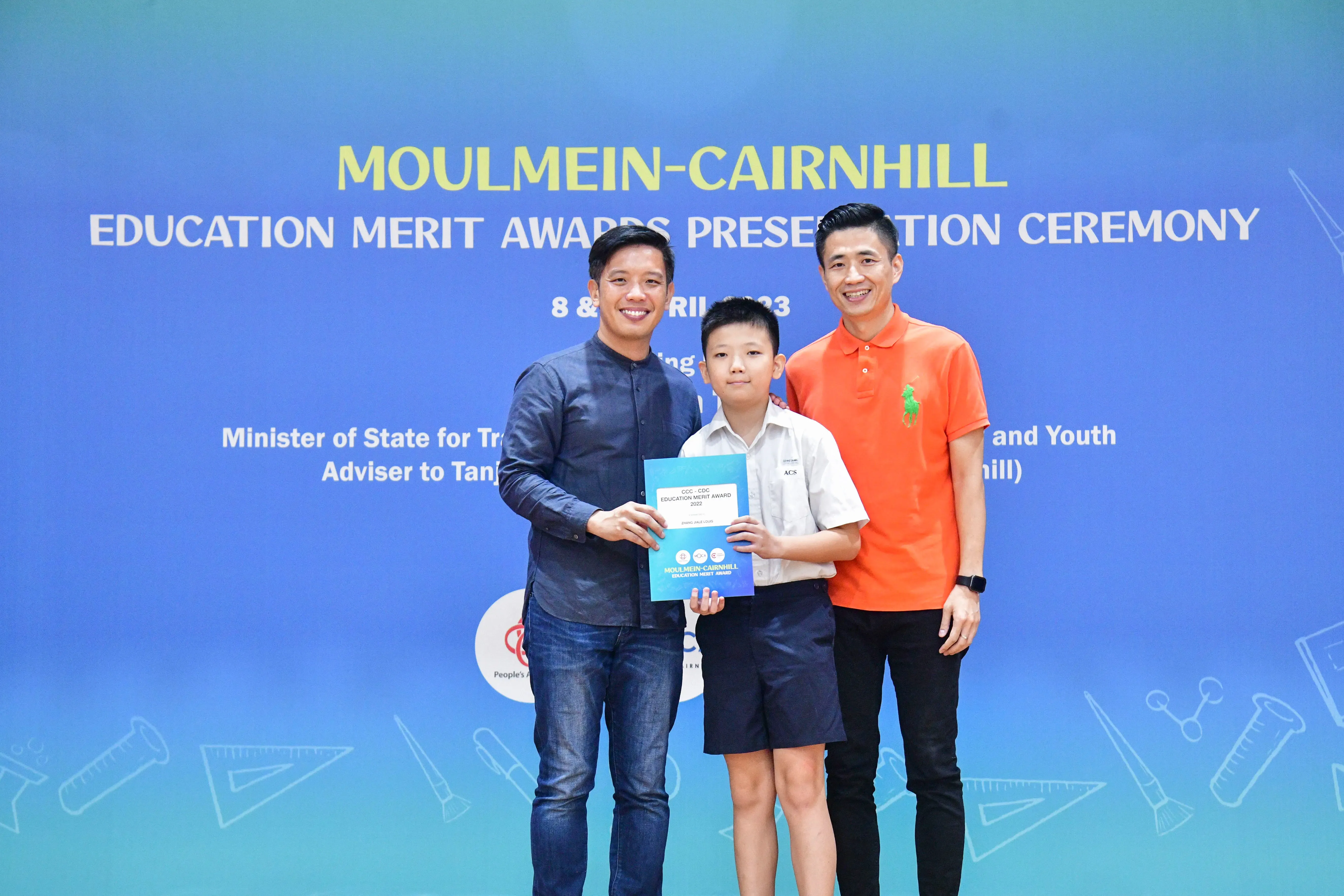 Two men and a boy hold a certificate at the Moulmein-Cairnhill Education Merit Awards Presentation Ceremony.