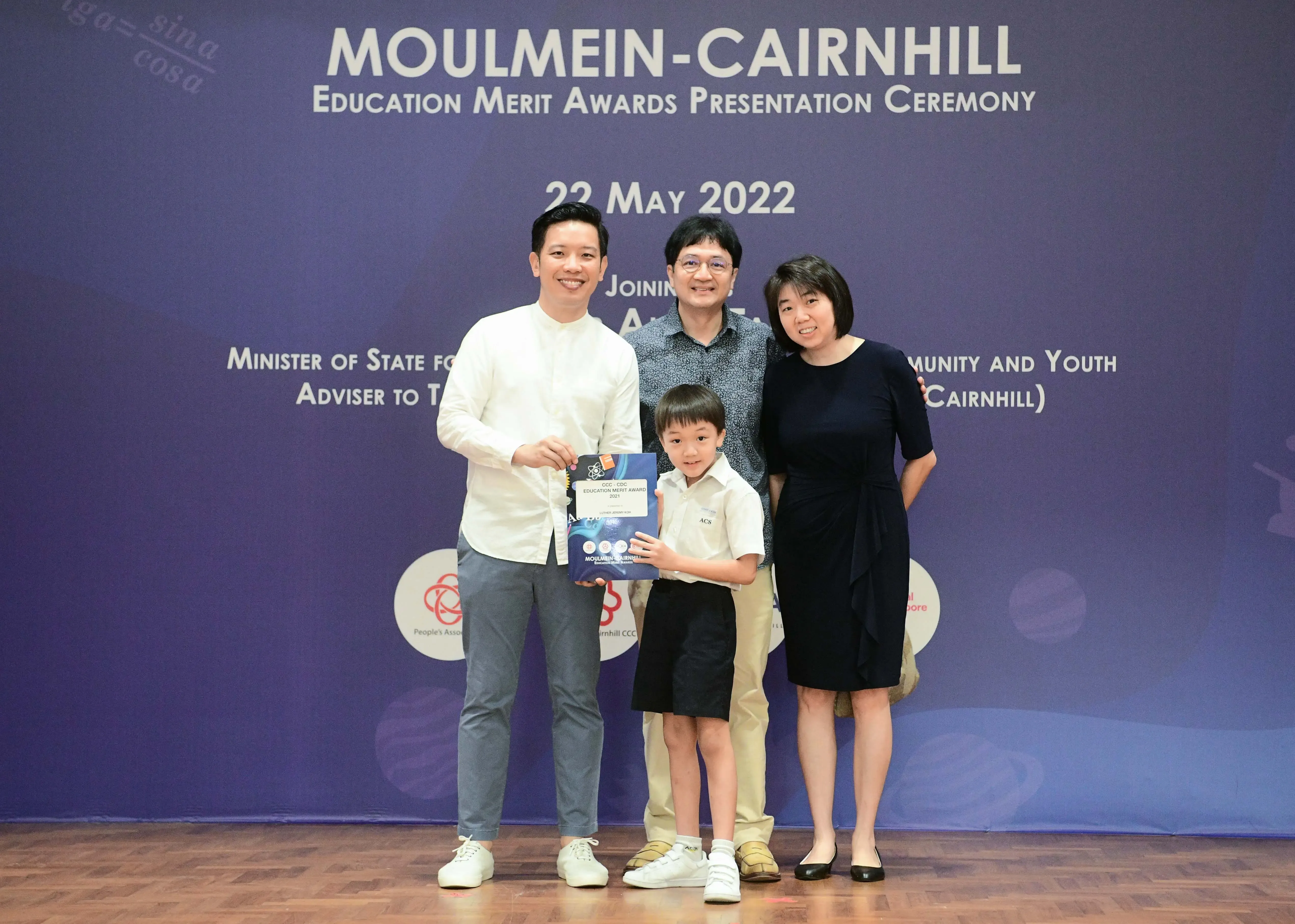 Three adults and a young boy pose with an award at the Moulmein-Cairnhill Education Merit Awards Ceremony, May 2022.