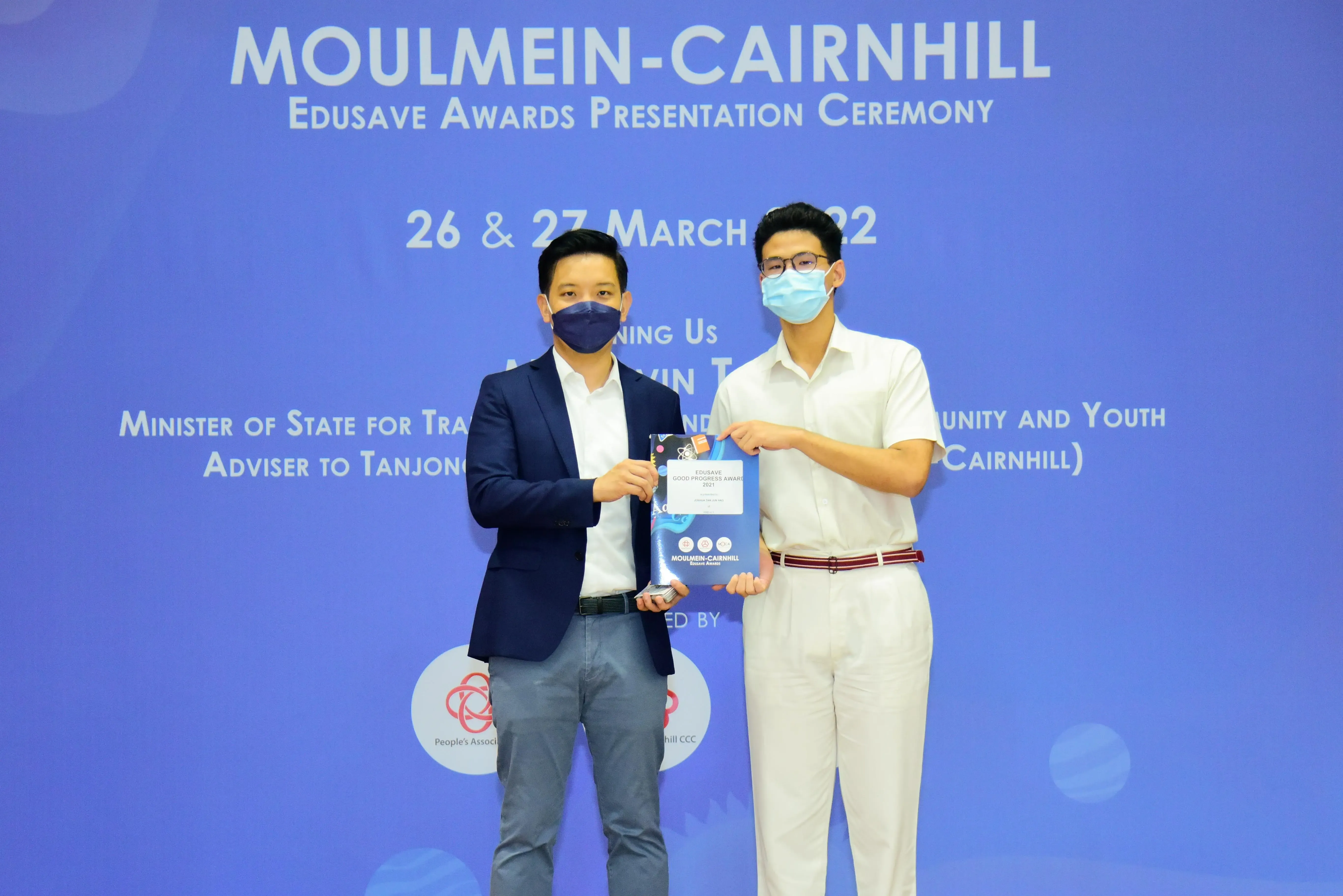 Two masked men hold an Edusave award certificate at the Moulmein-Cairnhill Edusave Awards Presentation Ceremony.