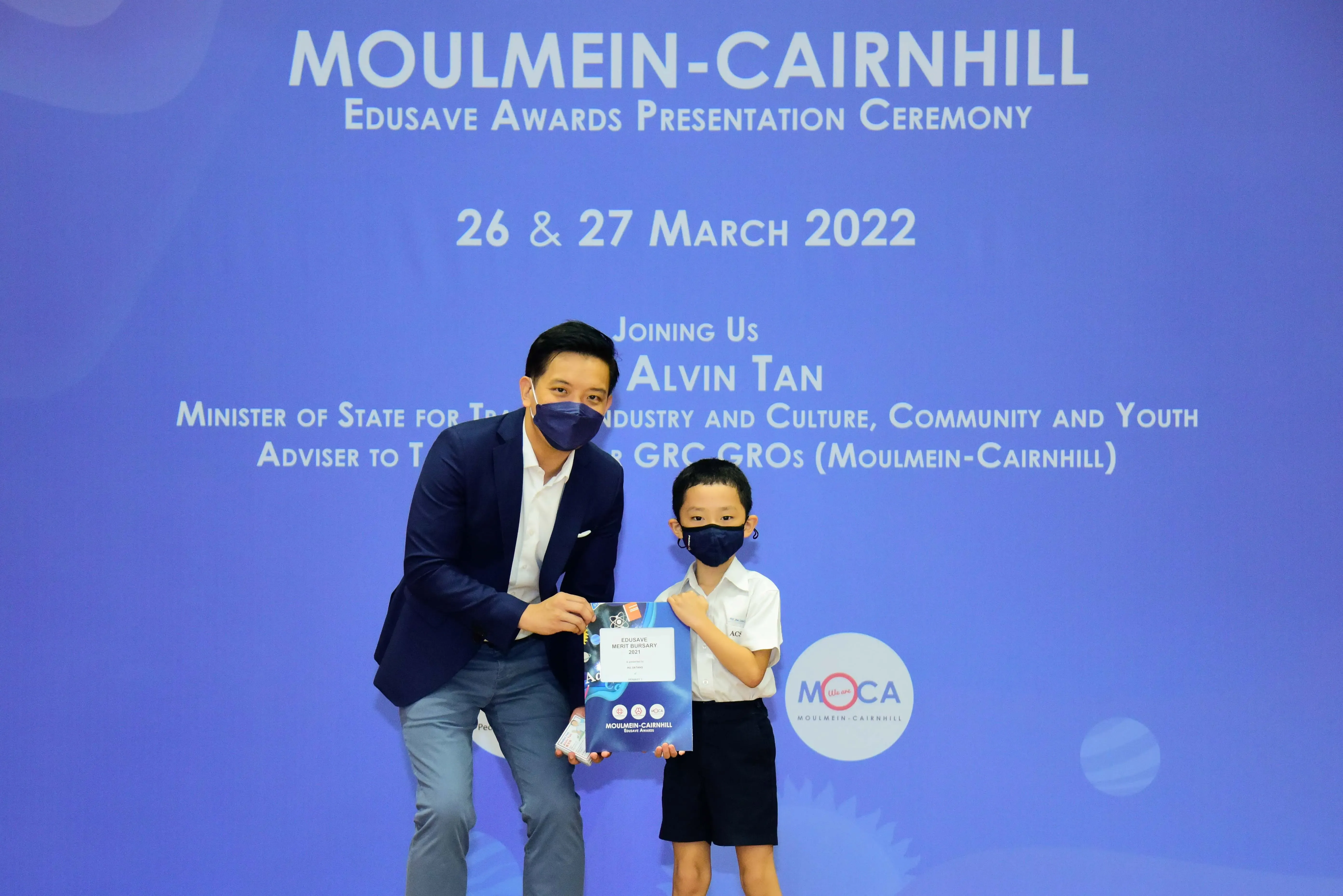 An adult and a young child in masks hold an award at the Moulmein-Cairnhill Edusave Awards Ceremony, March 2022.