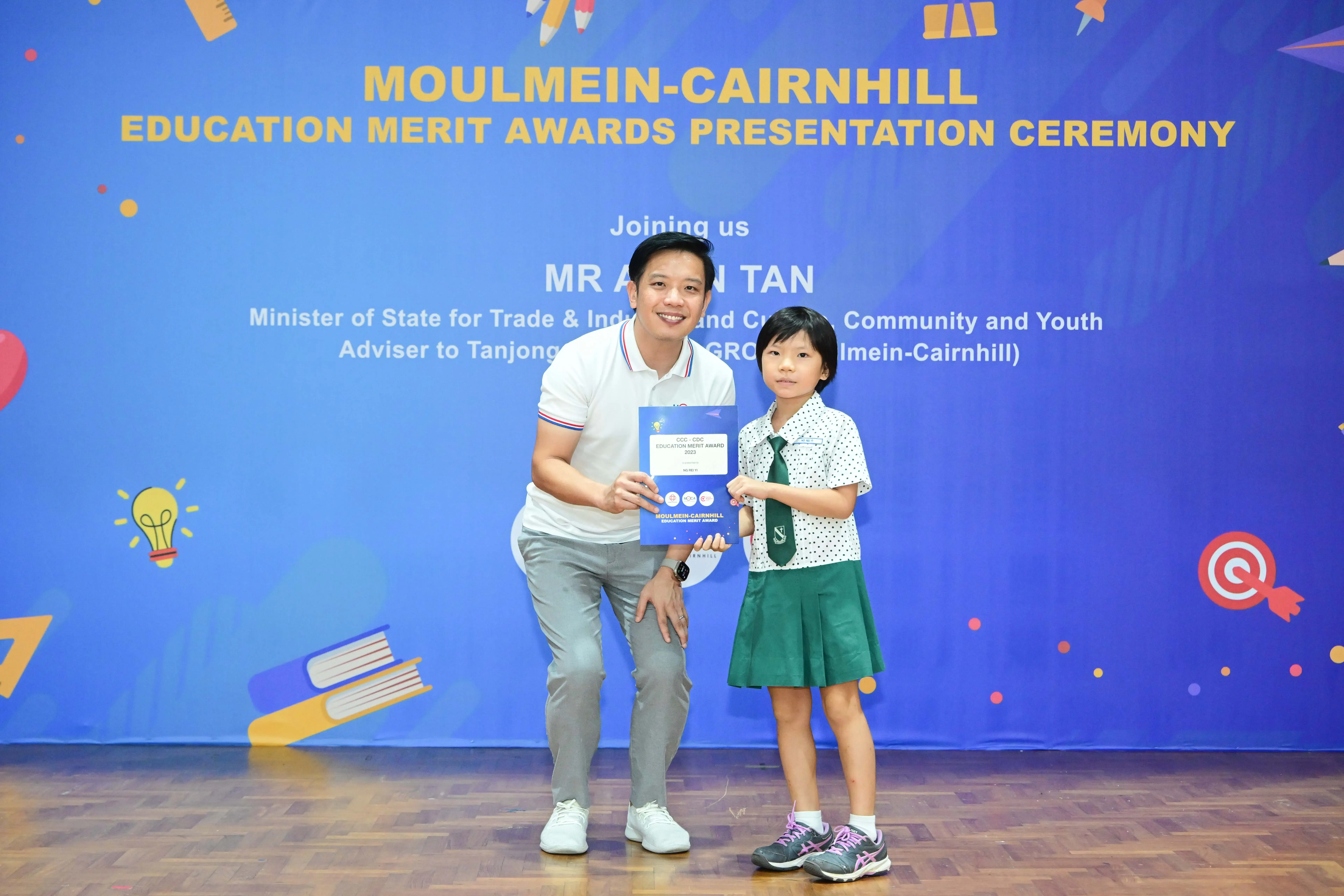 Man and young girl in school uniform hold an award certificate at Moulmein-Cairnhill Education Merit Awards ceremony.